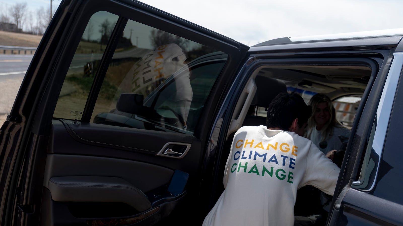 A young man climbs into the back of a car after a tree planting event. The back of his white shirt reads, “Change climate change.”