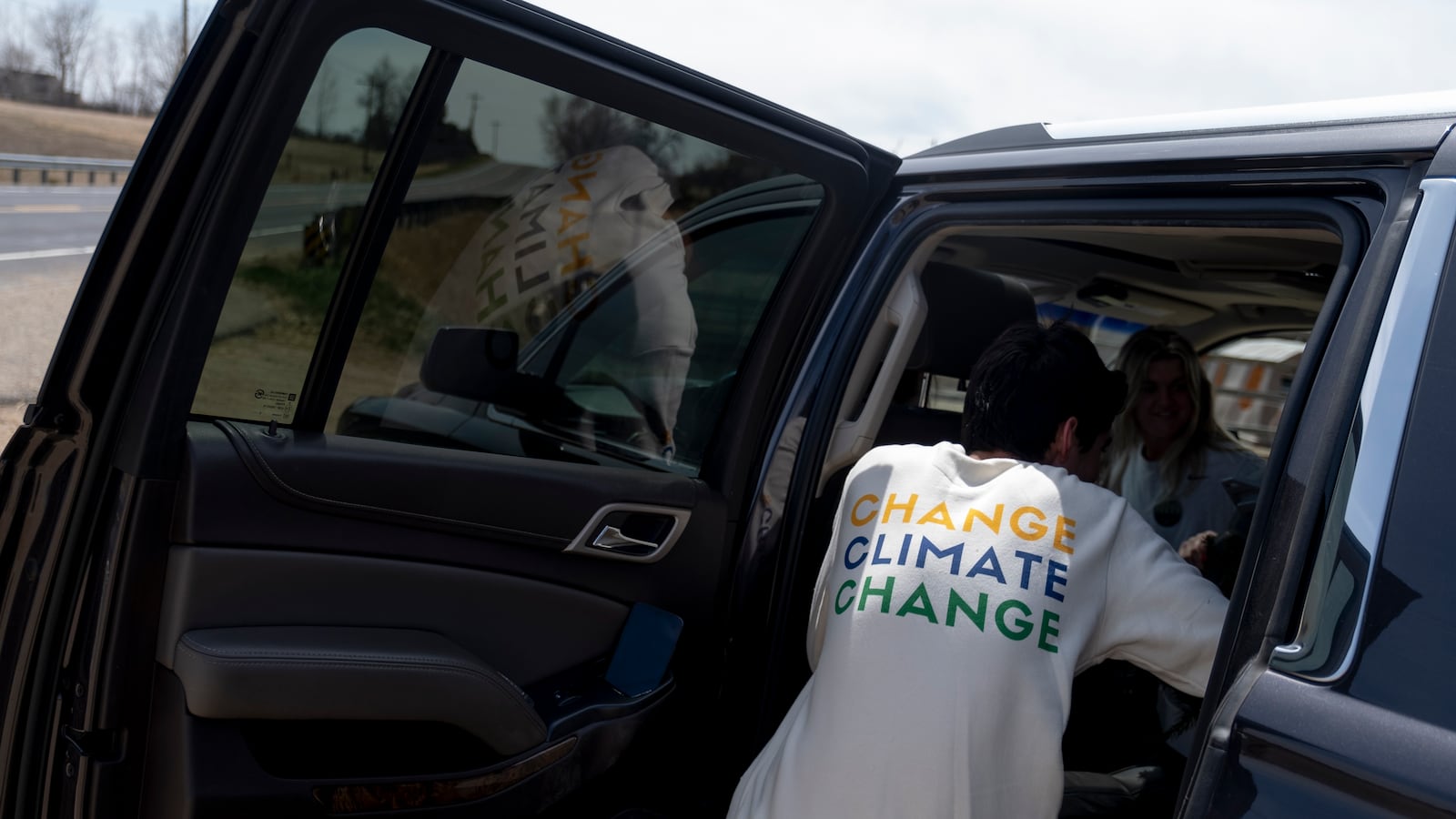 A young man climbs into the back of a car after a tree planting event. The back of his white shirt reads, “Change climate change.”