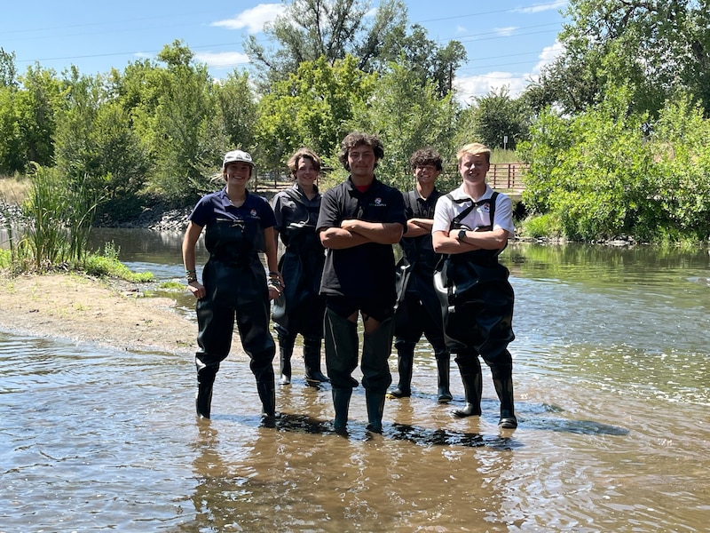 A photograph of a group of high school students standing in a river and posing for a portrait.