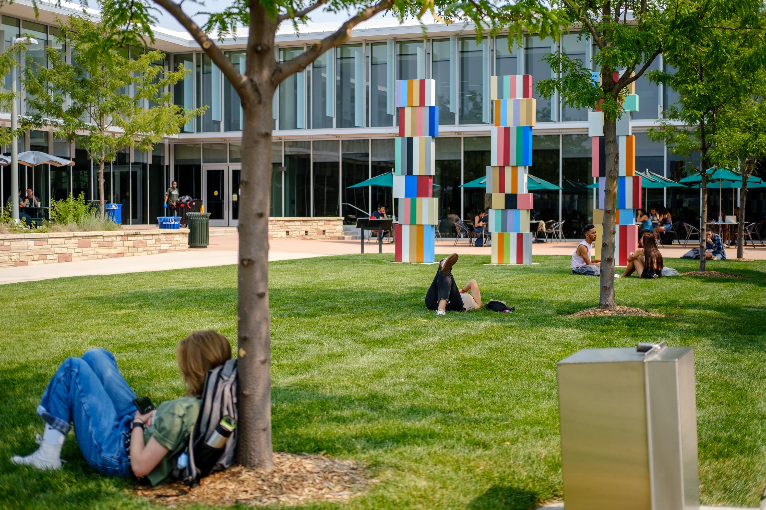 A couple of young adults sit in the grass with a large university in the background.