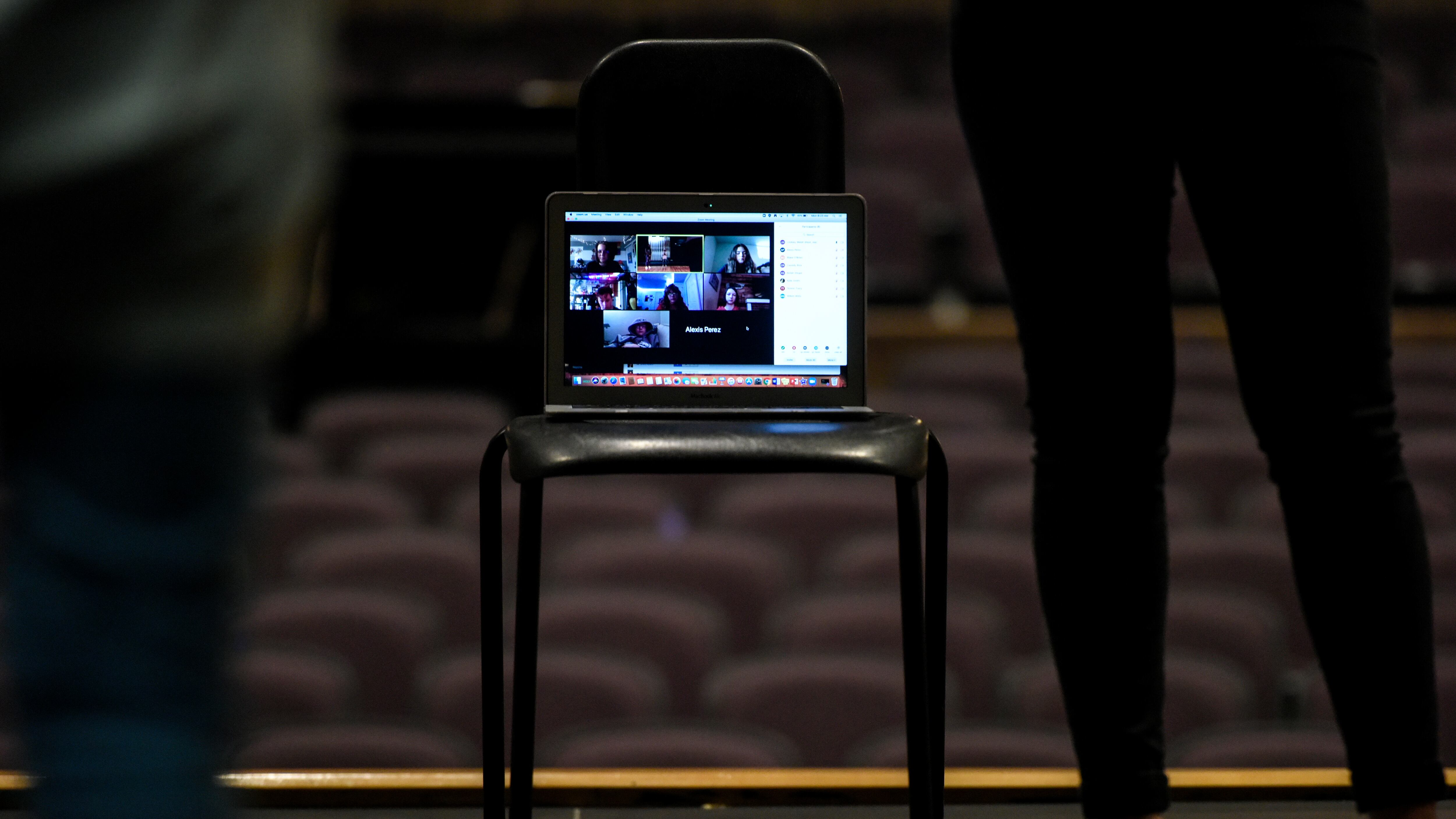 A laptop displaying a video call is perched on a chair on a stage.