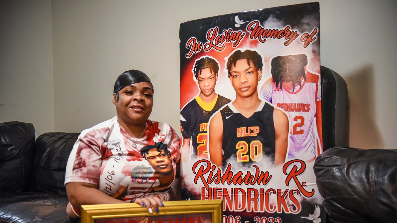 A mother holds a photo and a poster of her late son. The poster says, "In loving memory of Rishawn R. Hendricks."