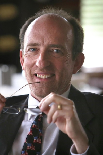 A man in a suit jacket holds his glasses