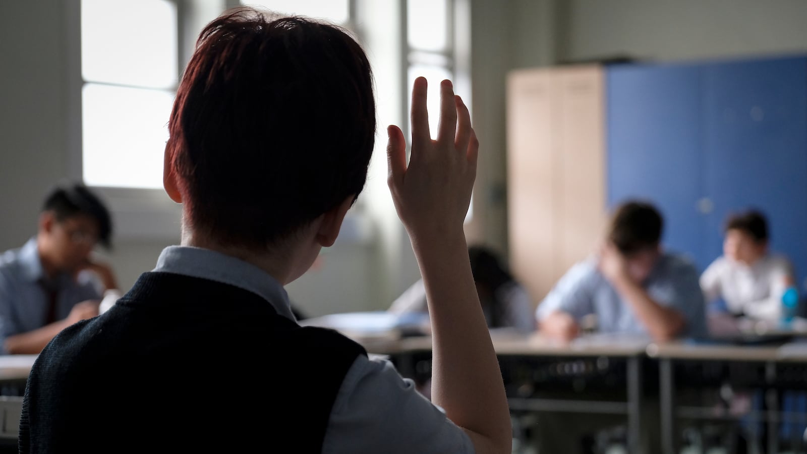 A student in uniform holds his hand up.