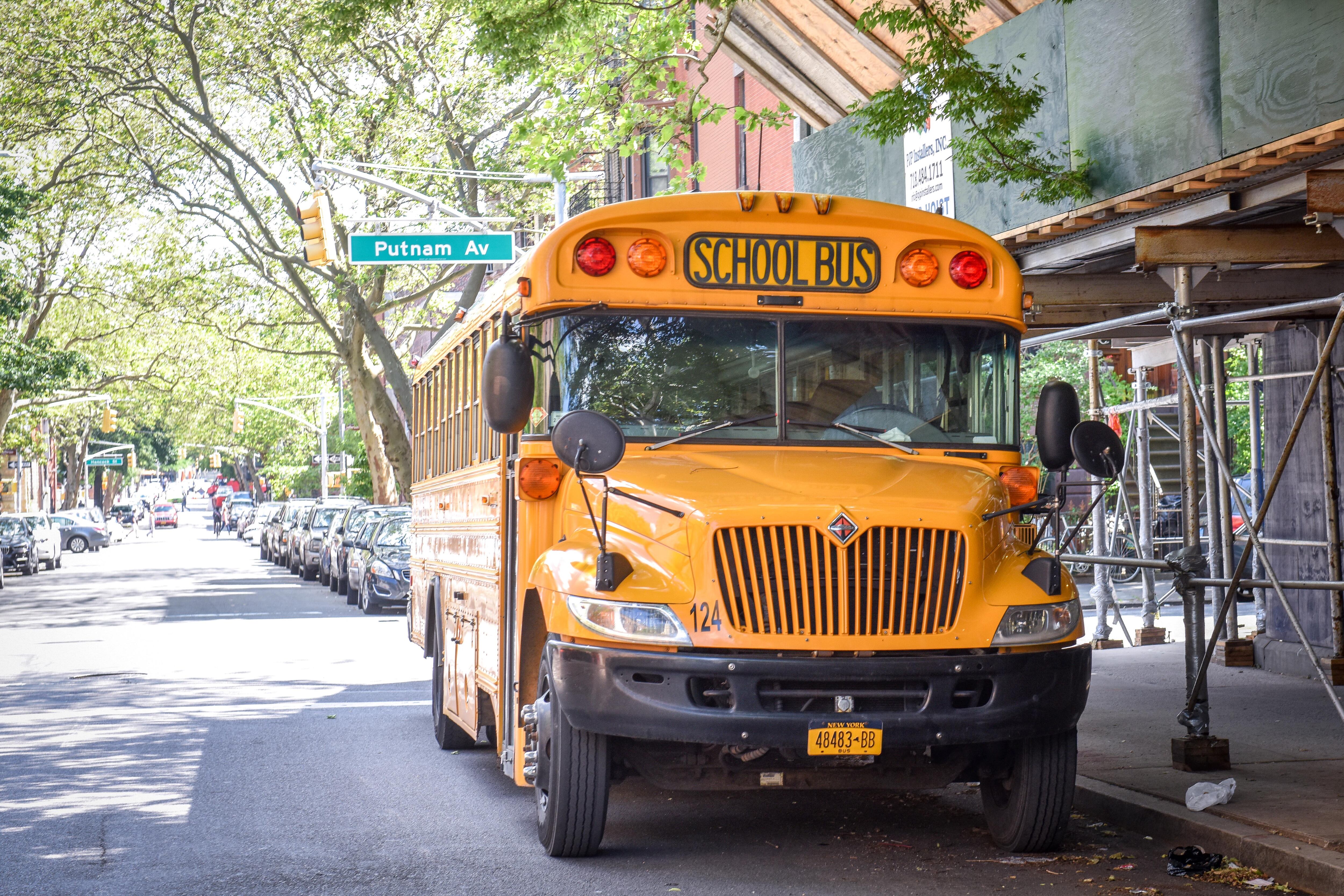 A yellow school bus is parked on the side of a street with scaffolding and buildings in the background.