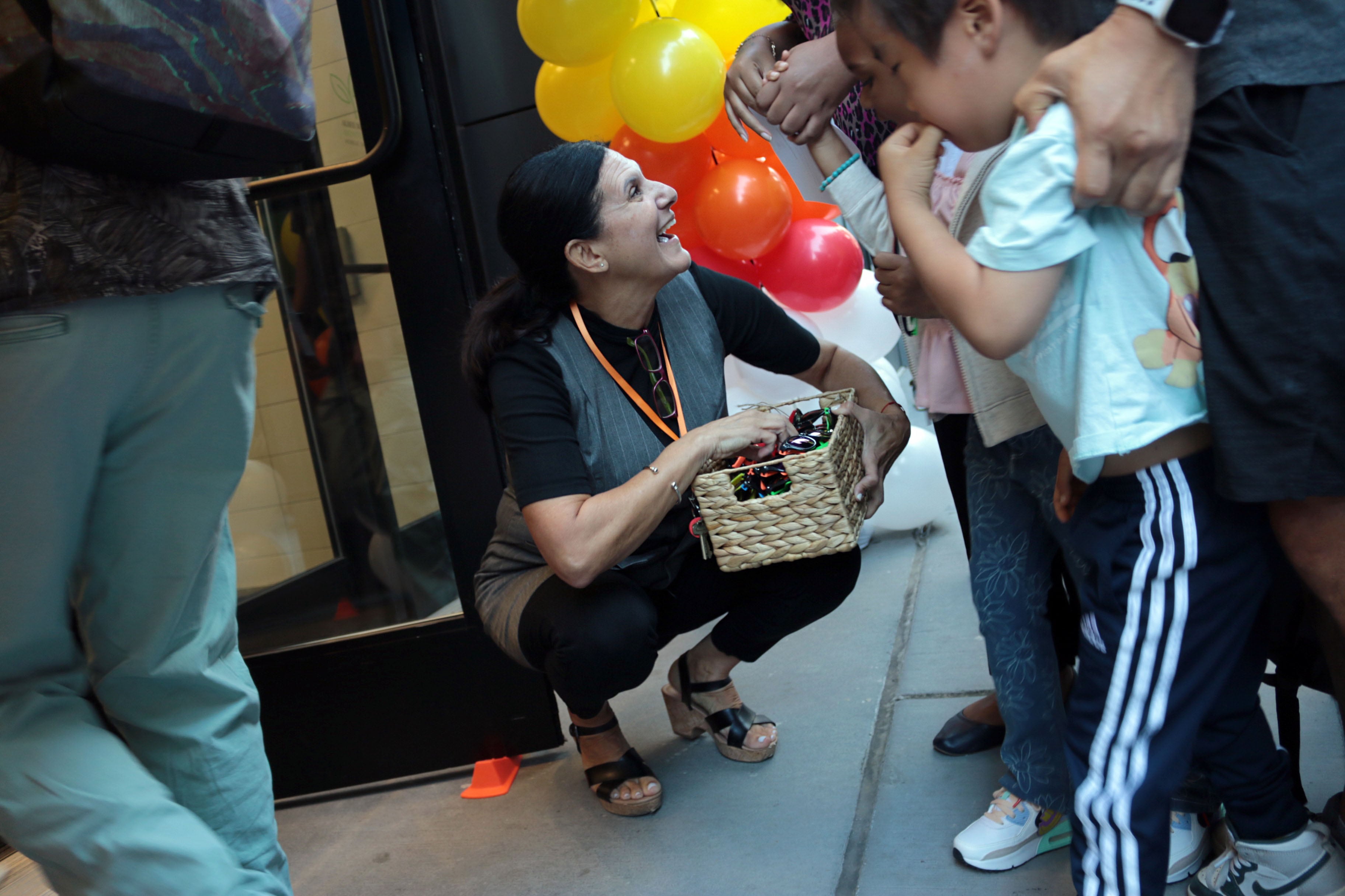 An adult kneels down in front of young students outside of a stone building.