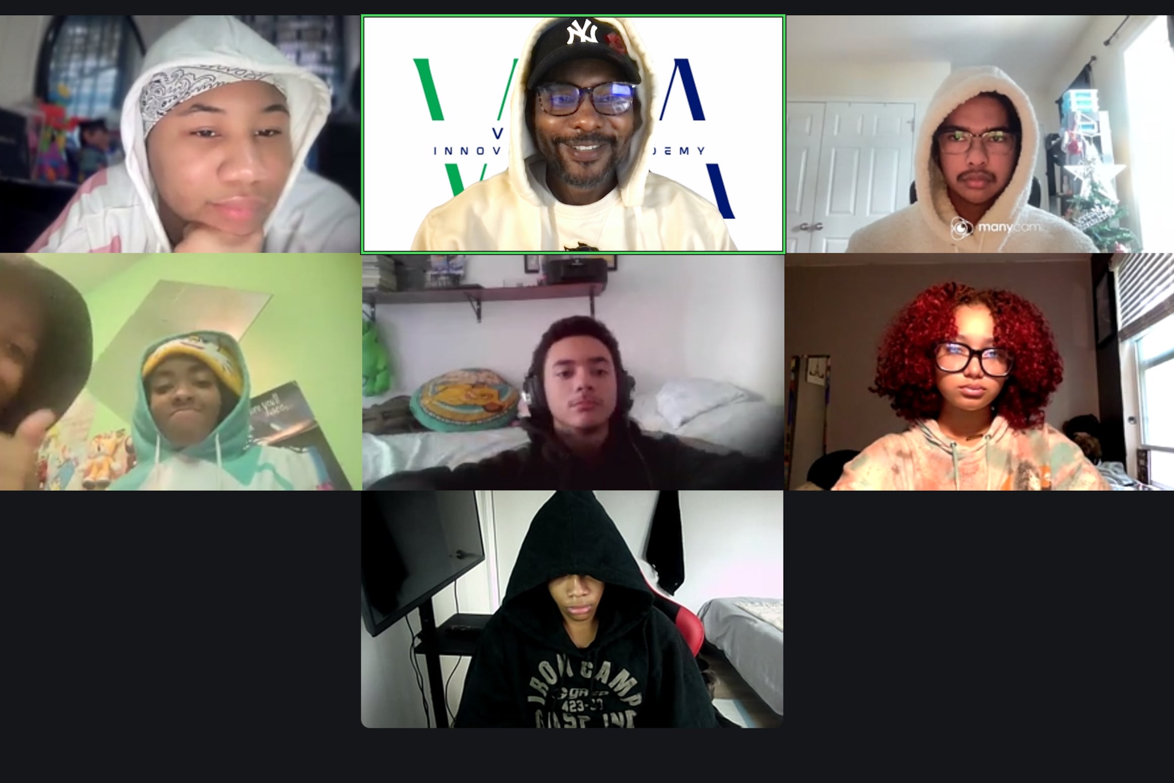 A screen grab of a virtual meeting room with seven squares on a black box. Each square has a student or a teacher and one square has two students posing for the virtual group photo.