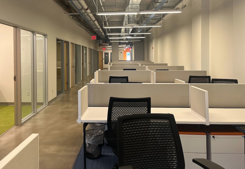 White desks line a hallway with glass doors on the left.