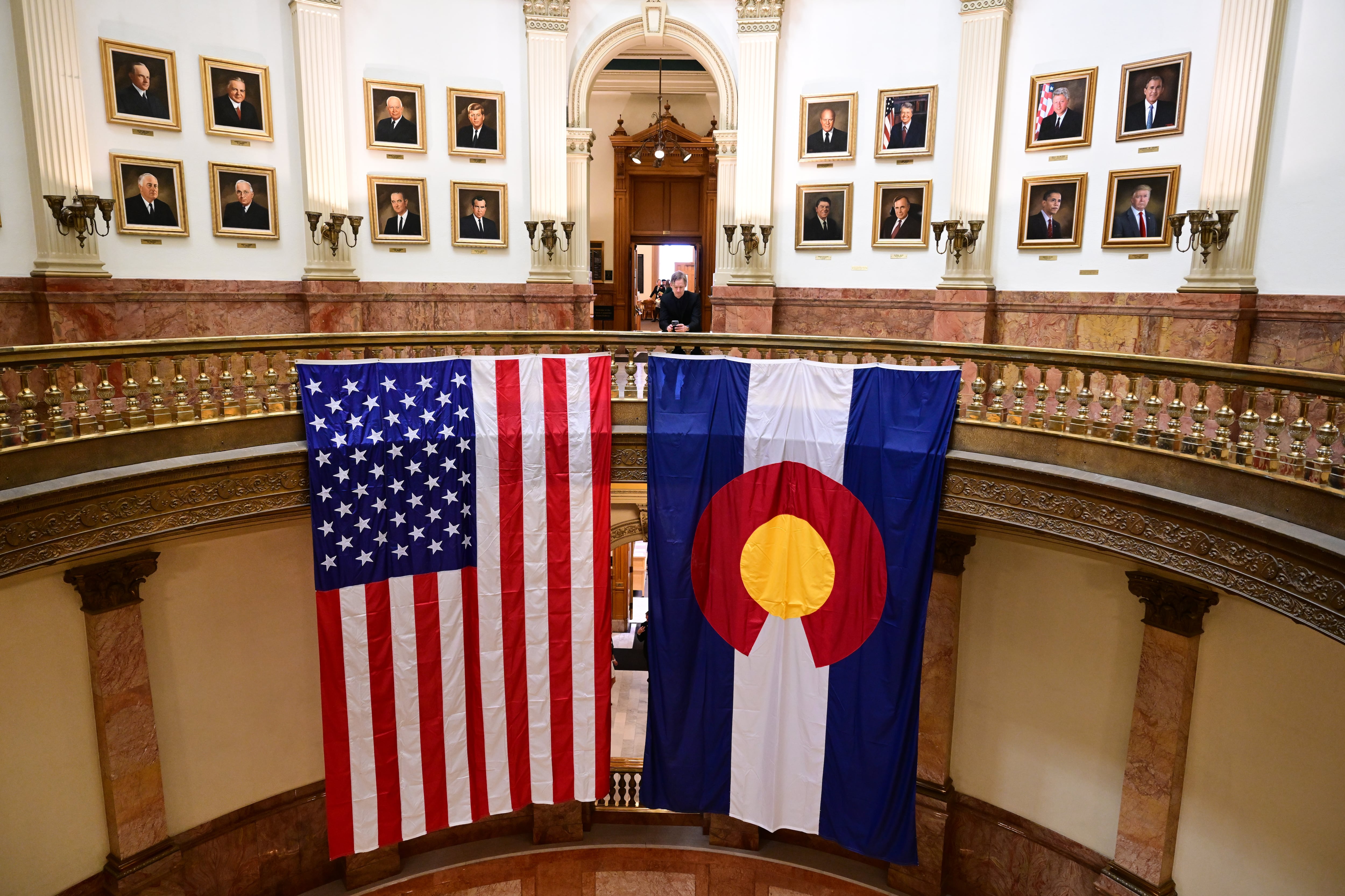 Enormous American and Colorado flags hang from the railing in the rotunda of the Colorado State Capitol. Portraits of past American presidents line the walls.