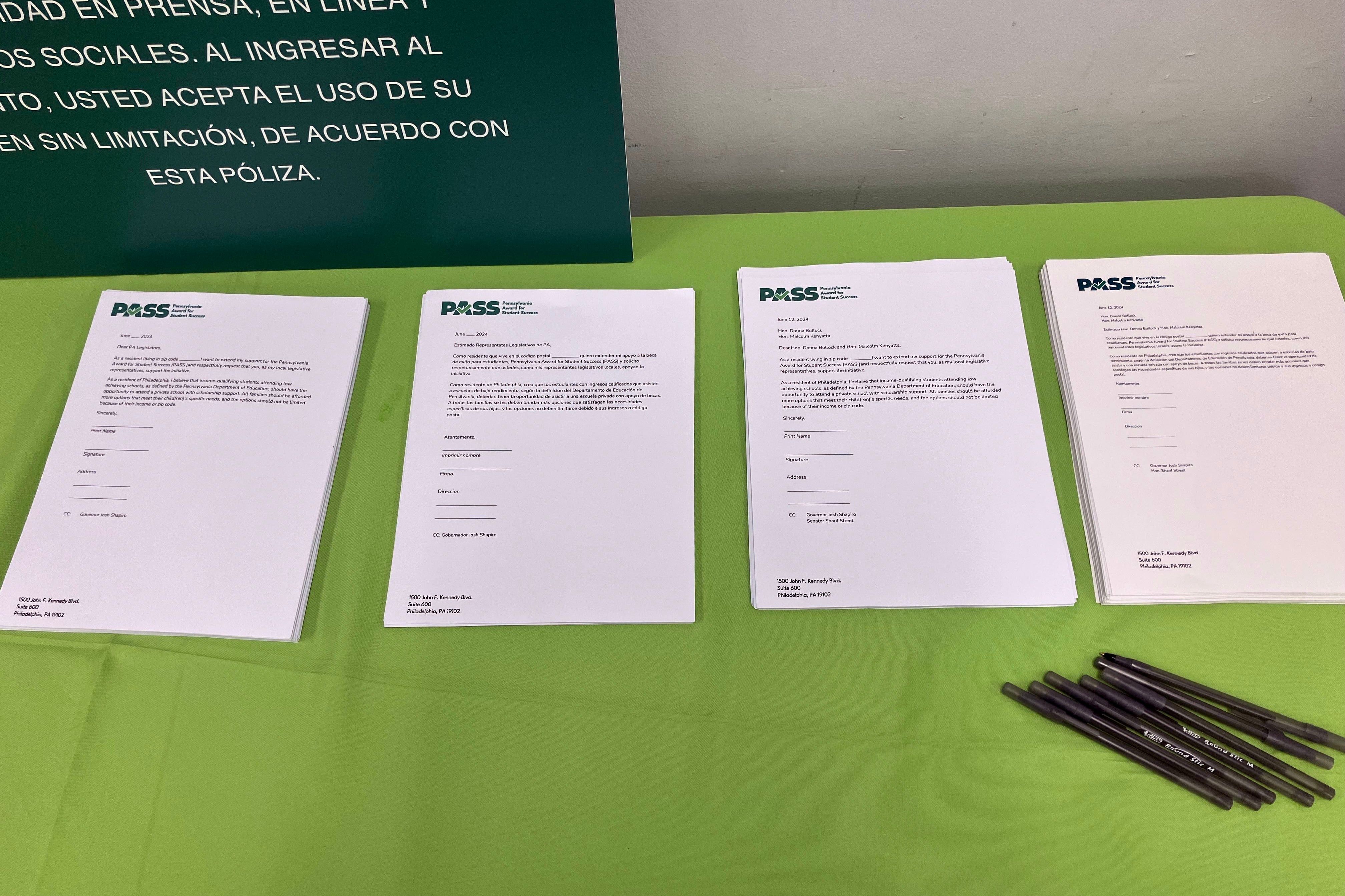 Four white pieces of paper with black ink sit on a table with a green table cloth and several black pens.