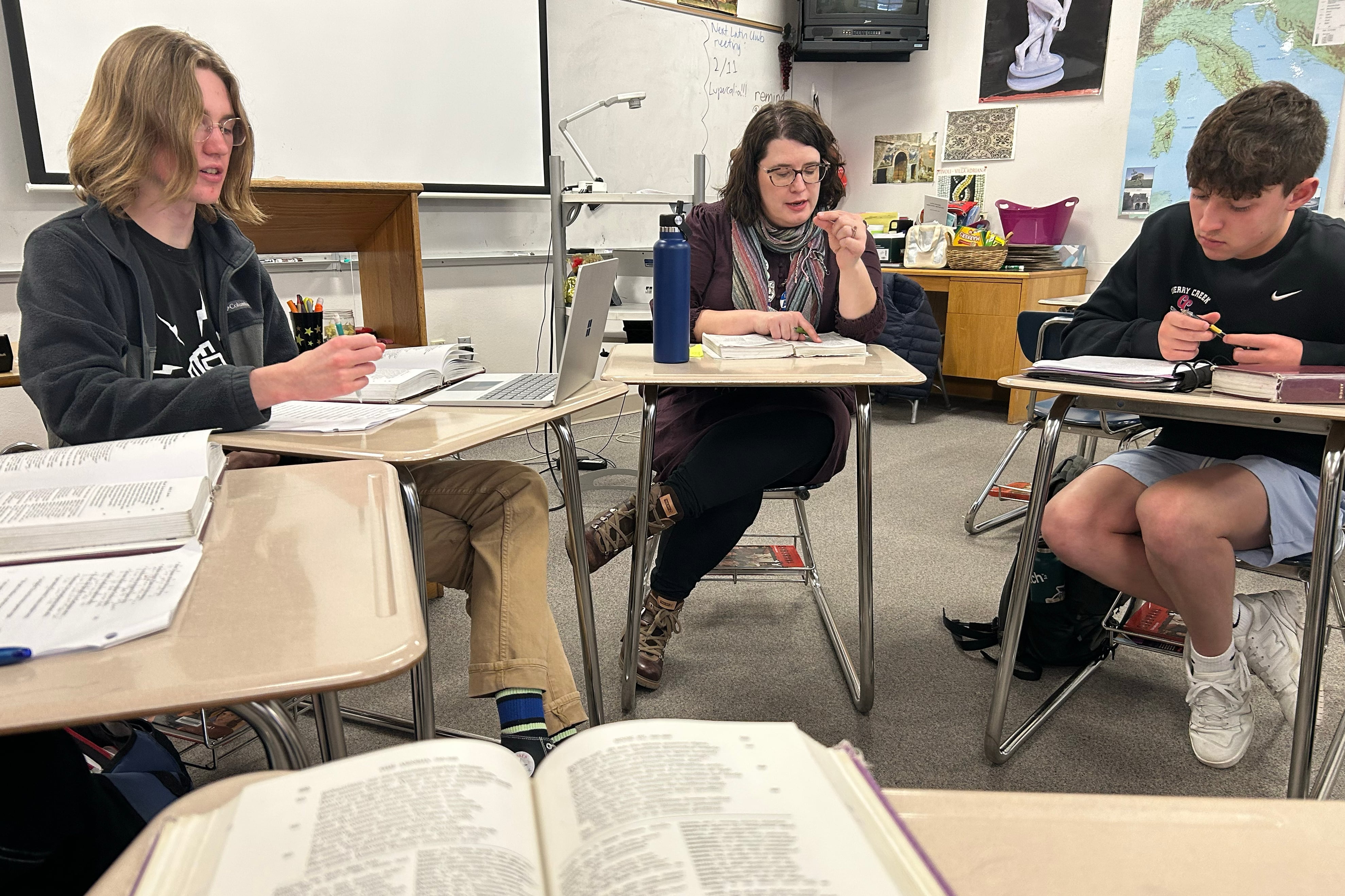 A teacher sits in between two high school students in a classroom.