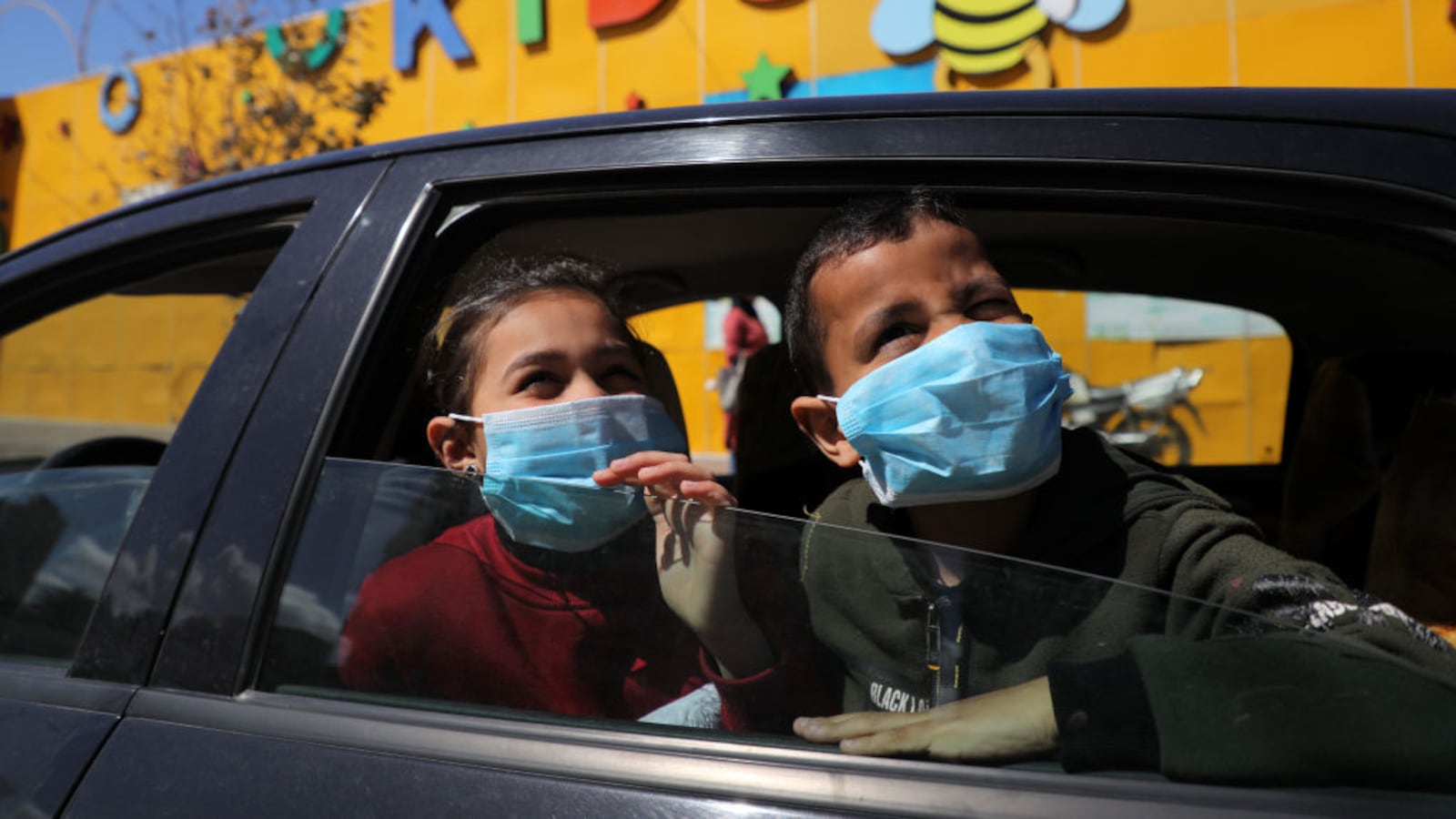 Palestinian children wearing masks look out of a car window in Gaza City on March 7, 2020, following a government decision to suspend schools due to fears of the spread of COVID-19.
