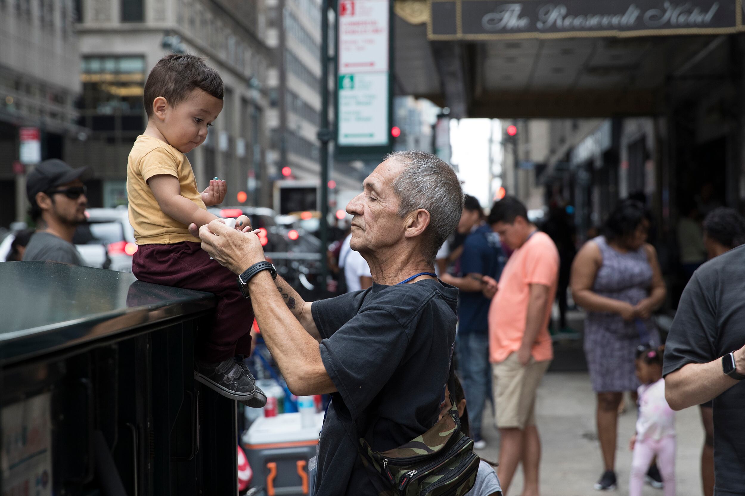 A man in a gray shirt faces a toddler in an orange shirt.