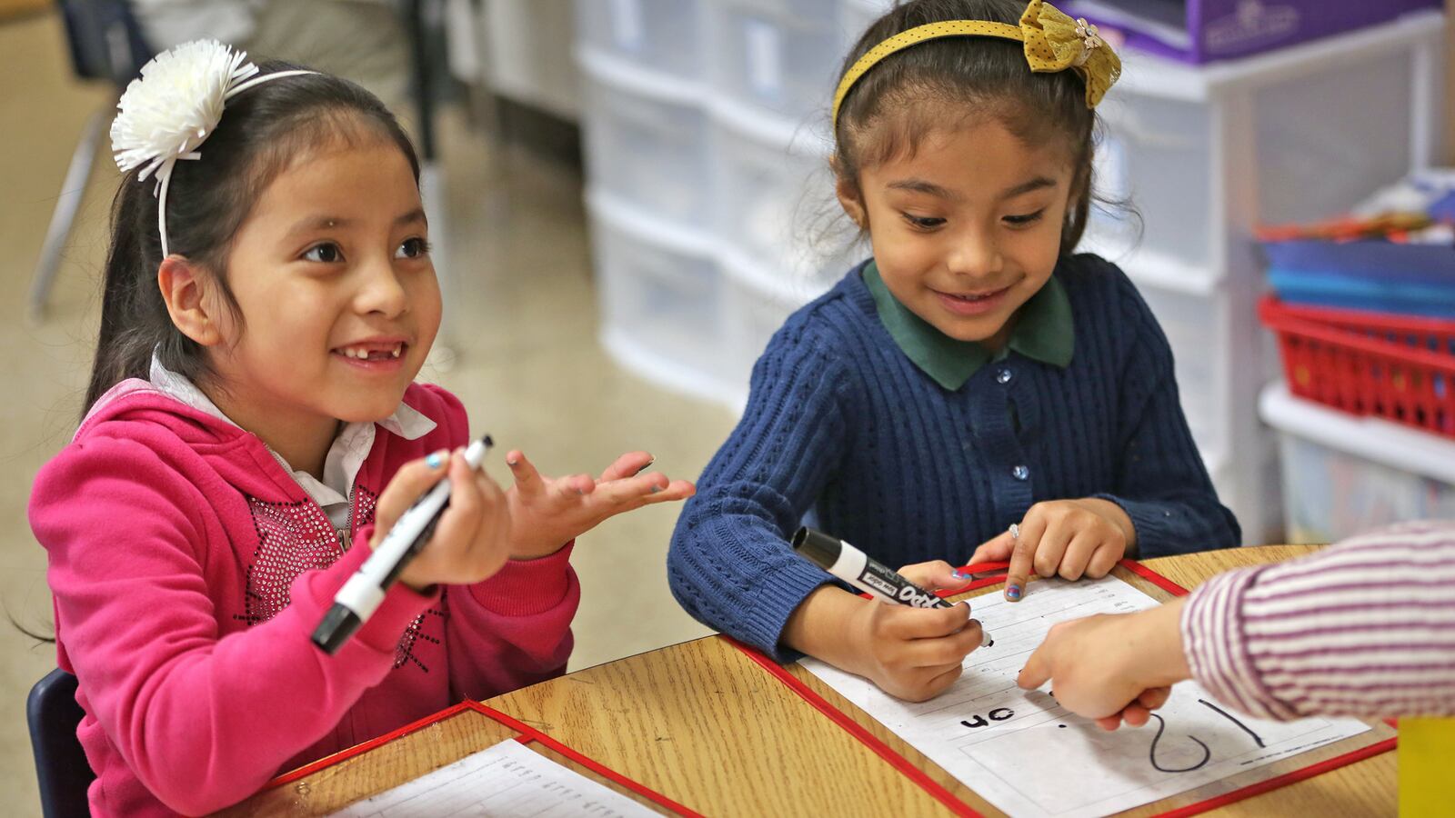 Kindergartners Ivania, left, and Jackie work on reading and writing with their teacher, Liz Amadio, at Enlace Academy.