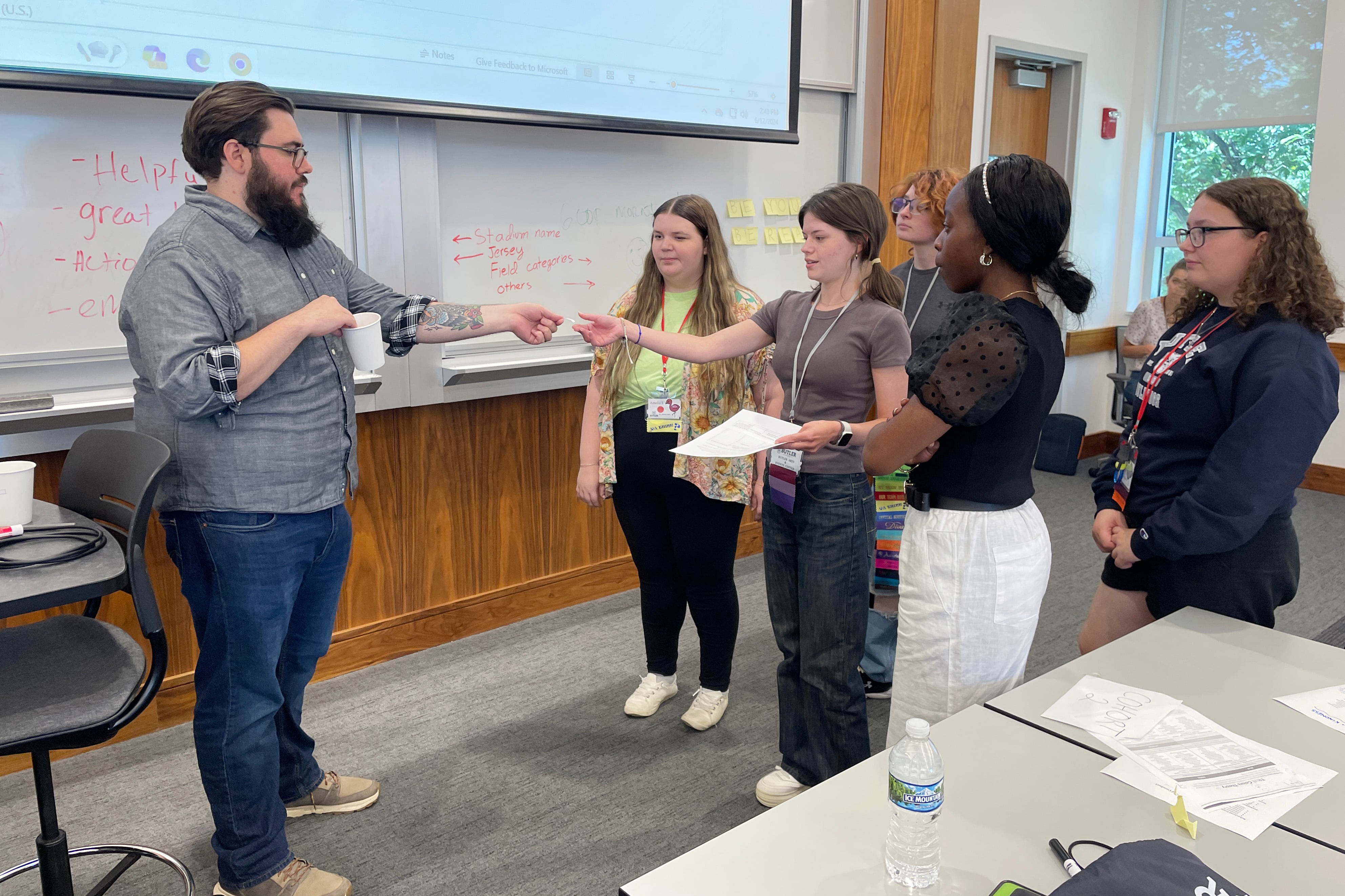 A man with a beard and glasses talks to students.