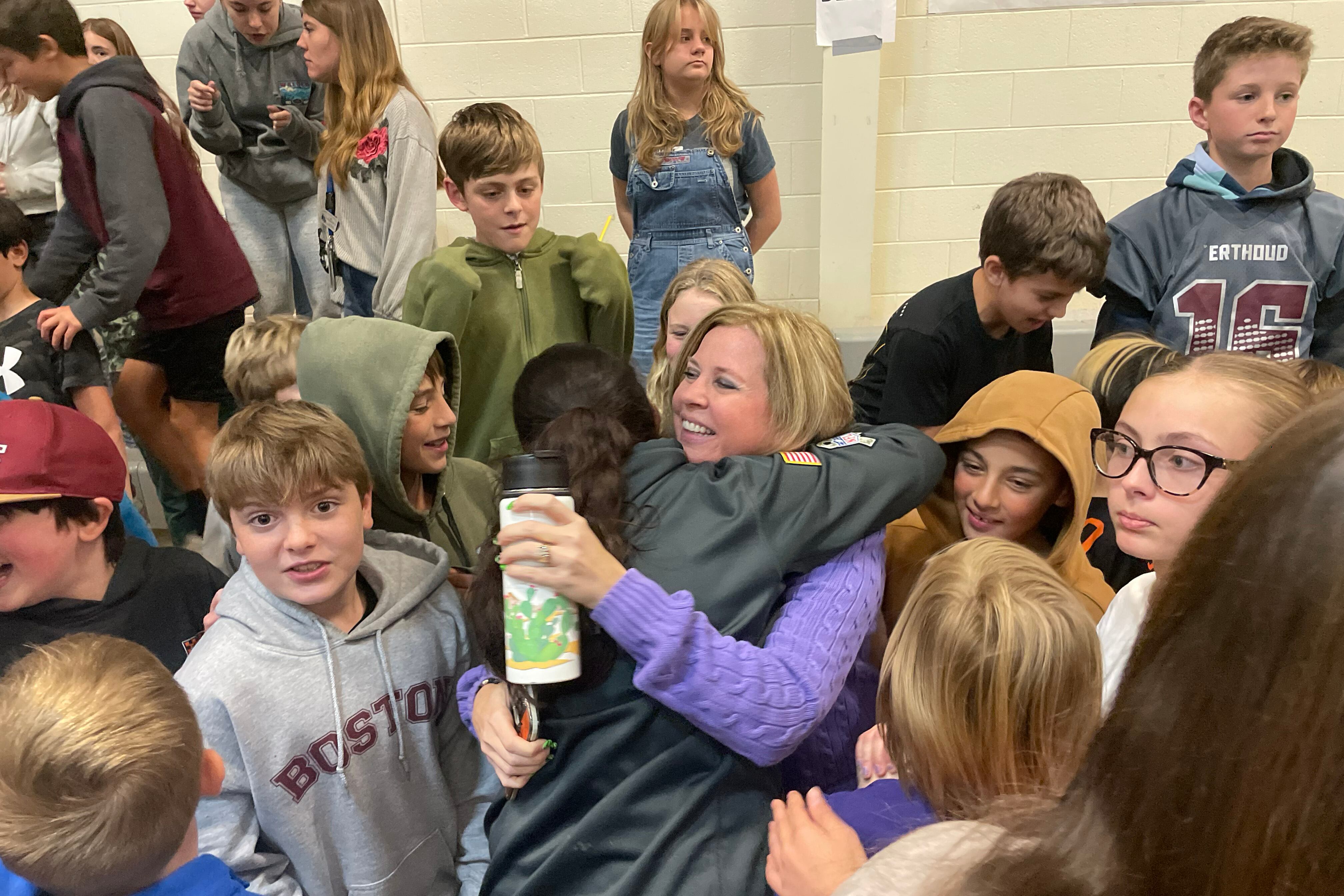 A woman in a purple sweater hugs a students while surrounded by other students.