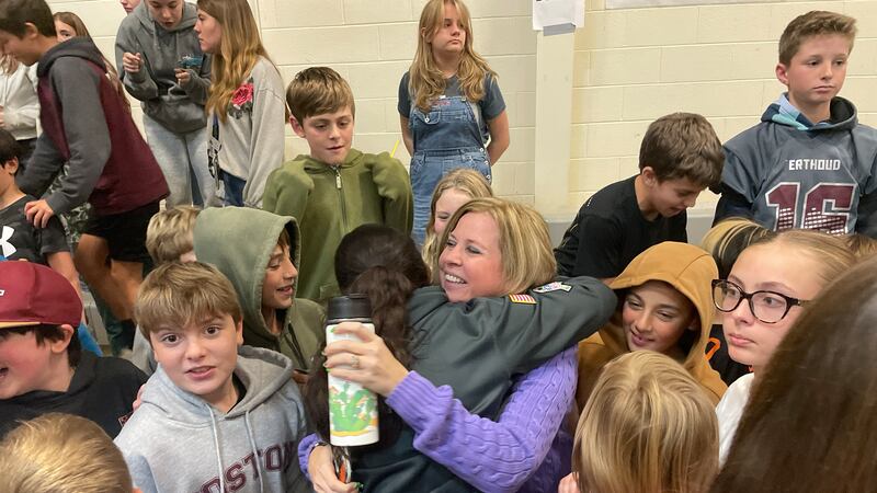 A woman in a purple sweater hugs a students while surrounded by other students.