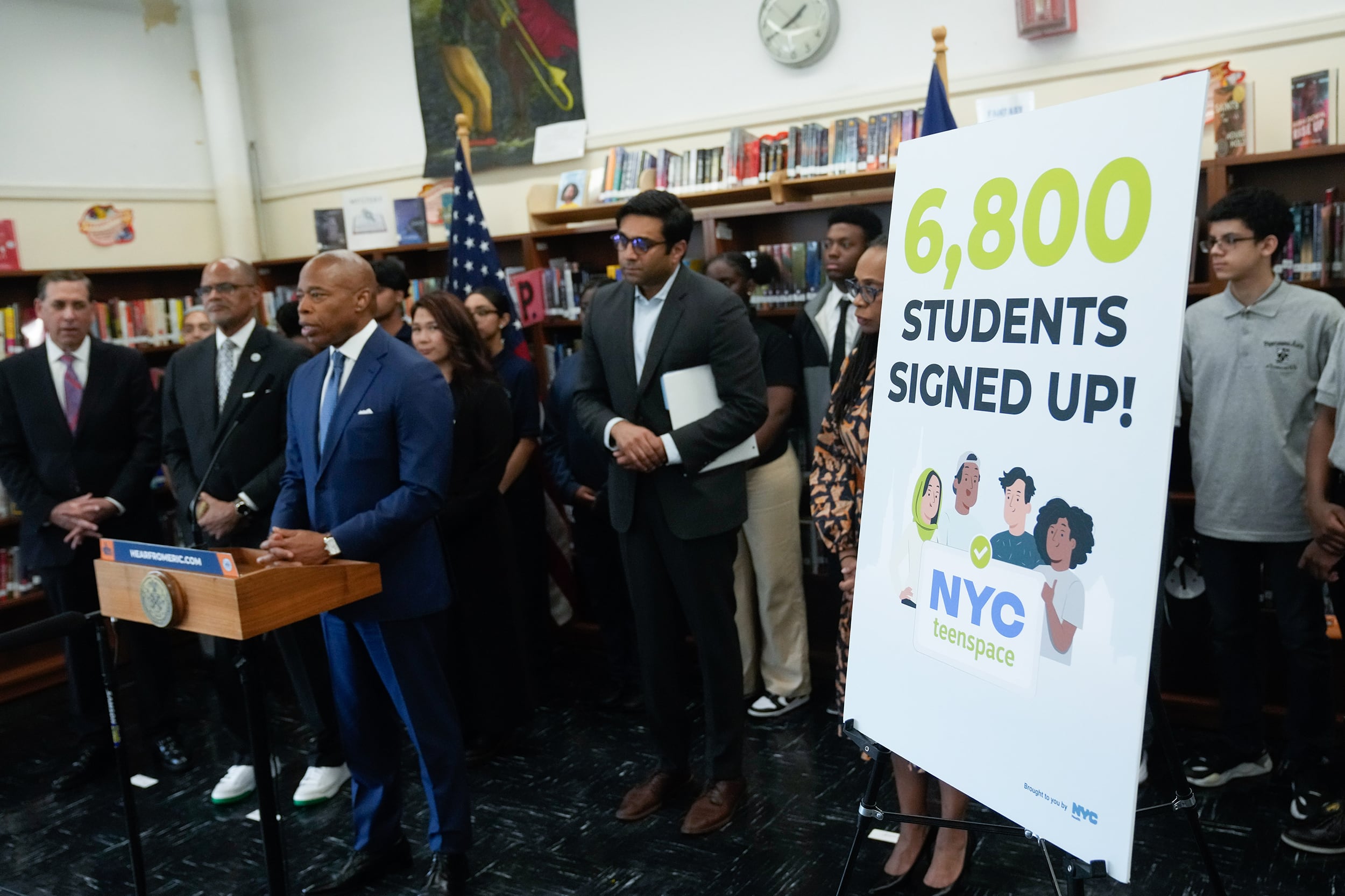 A group of people in business clothes stand in a library next to a large sign.