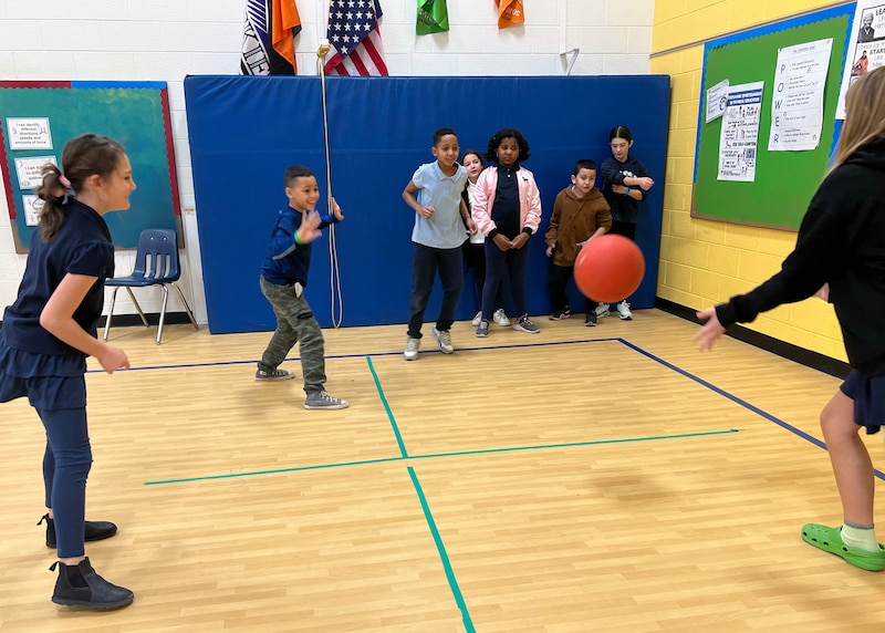 A group of students and a teacher play foursquare in a school gym.