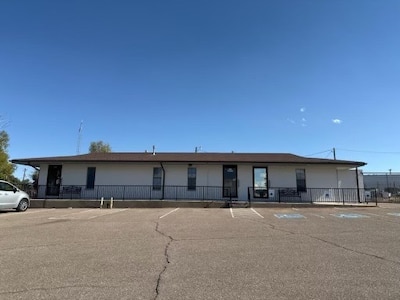 A one-story white building in front of a big asphalt parking lot