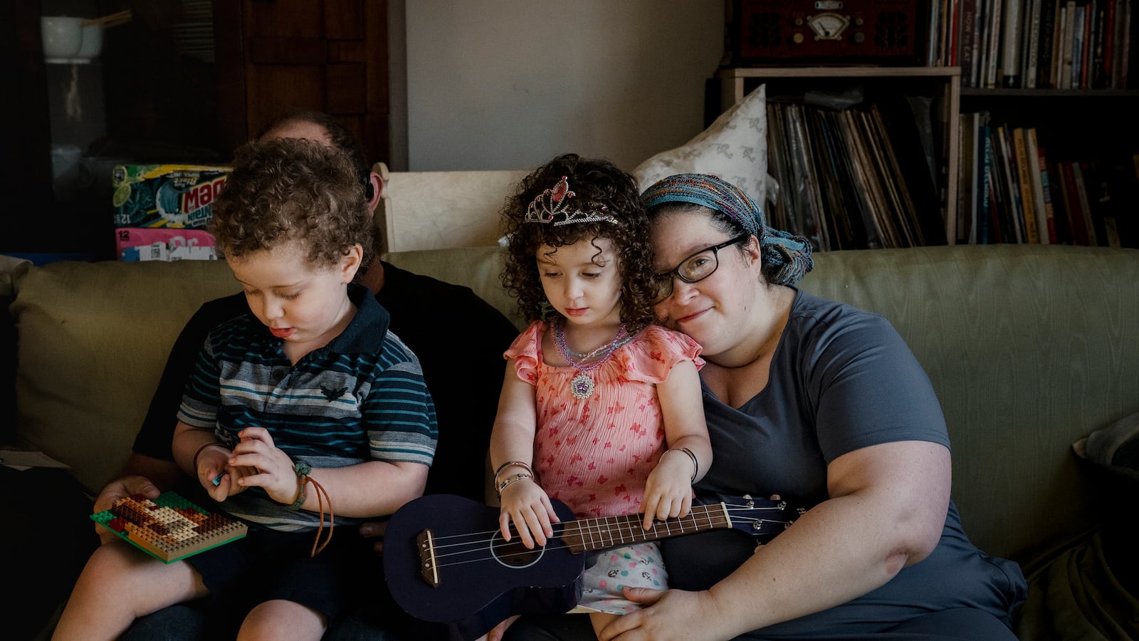 A photograph of two adult parents holding two young children posing for a photograph on a green sofa.