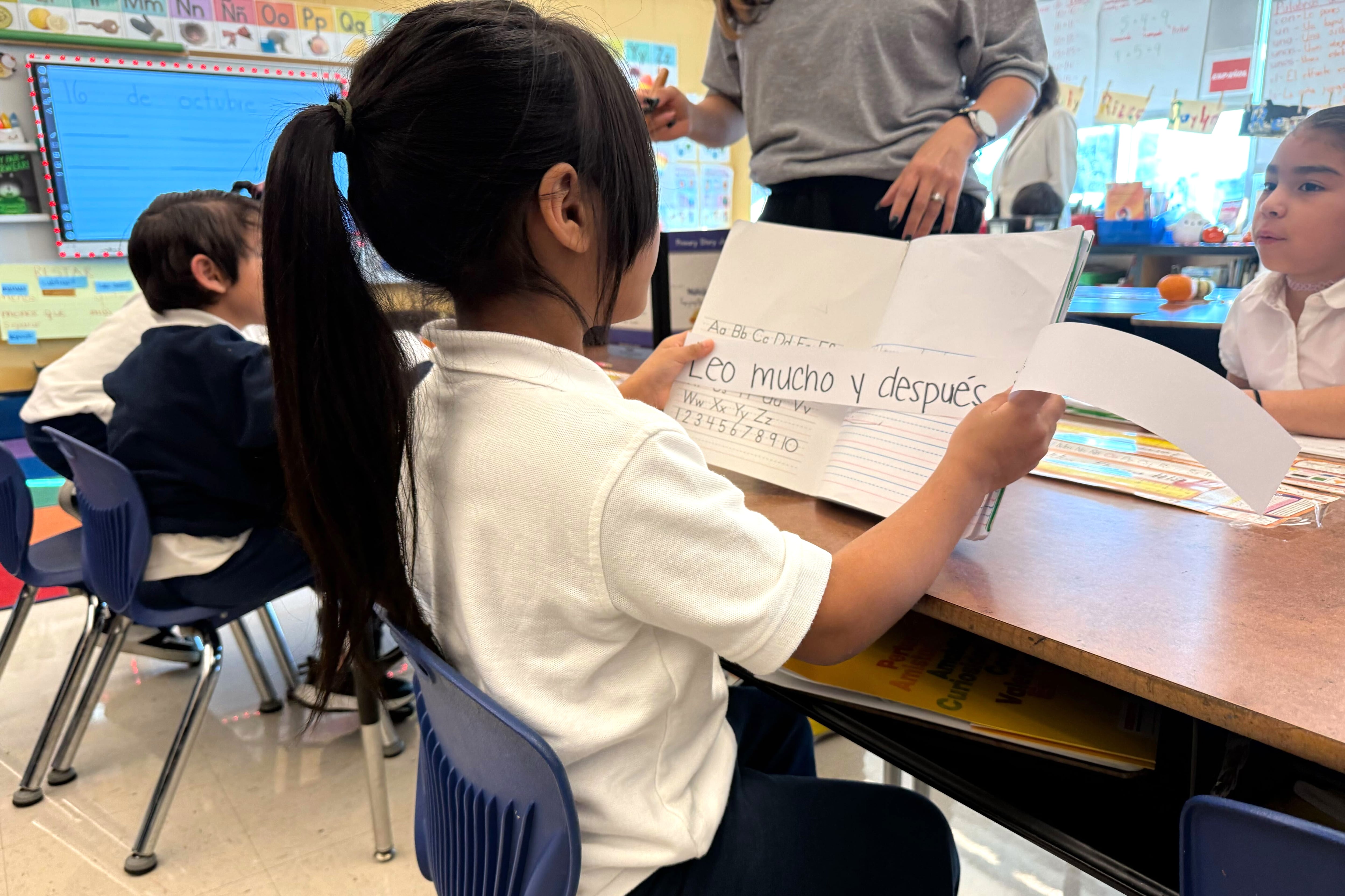 A girl with a white top and a pontyal holds a paper with Spanish words.