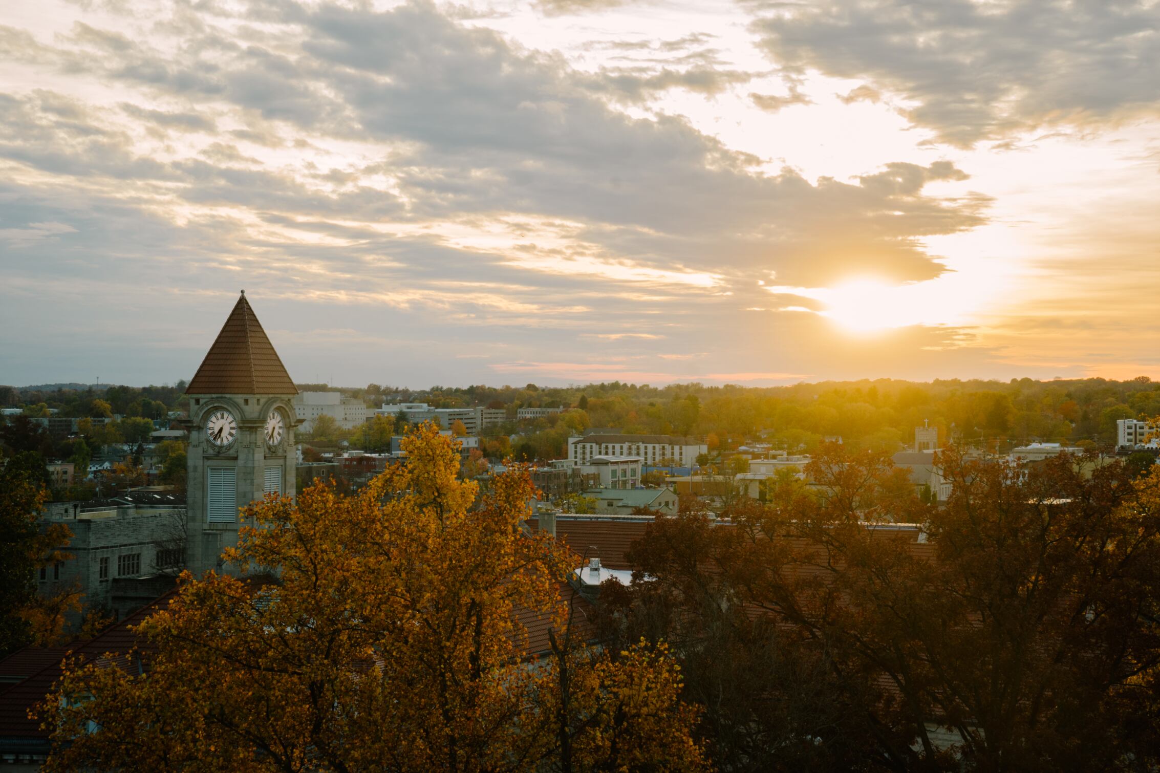 The sun shines over trees and buildings.