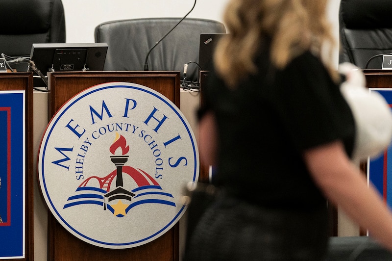 A photograph of a sign on a wooden desk with a person walking in the foreground.