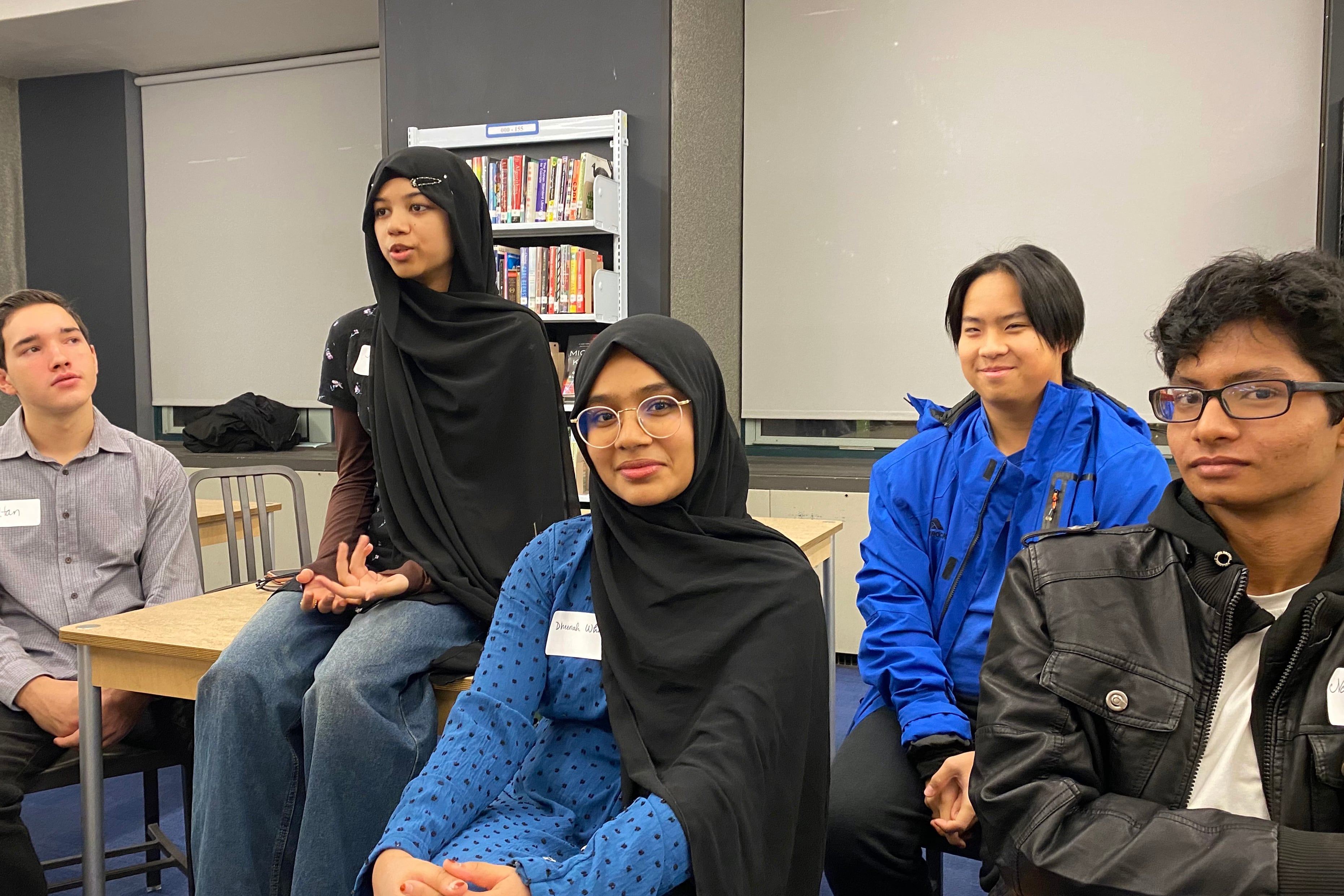 A group of high school students sit in an empty classroom posing for a photograph.
