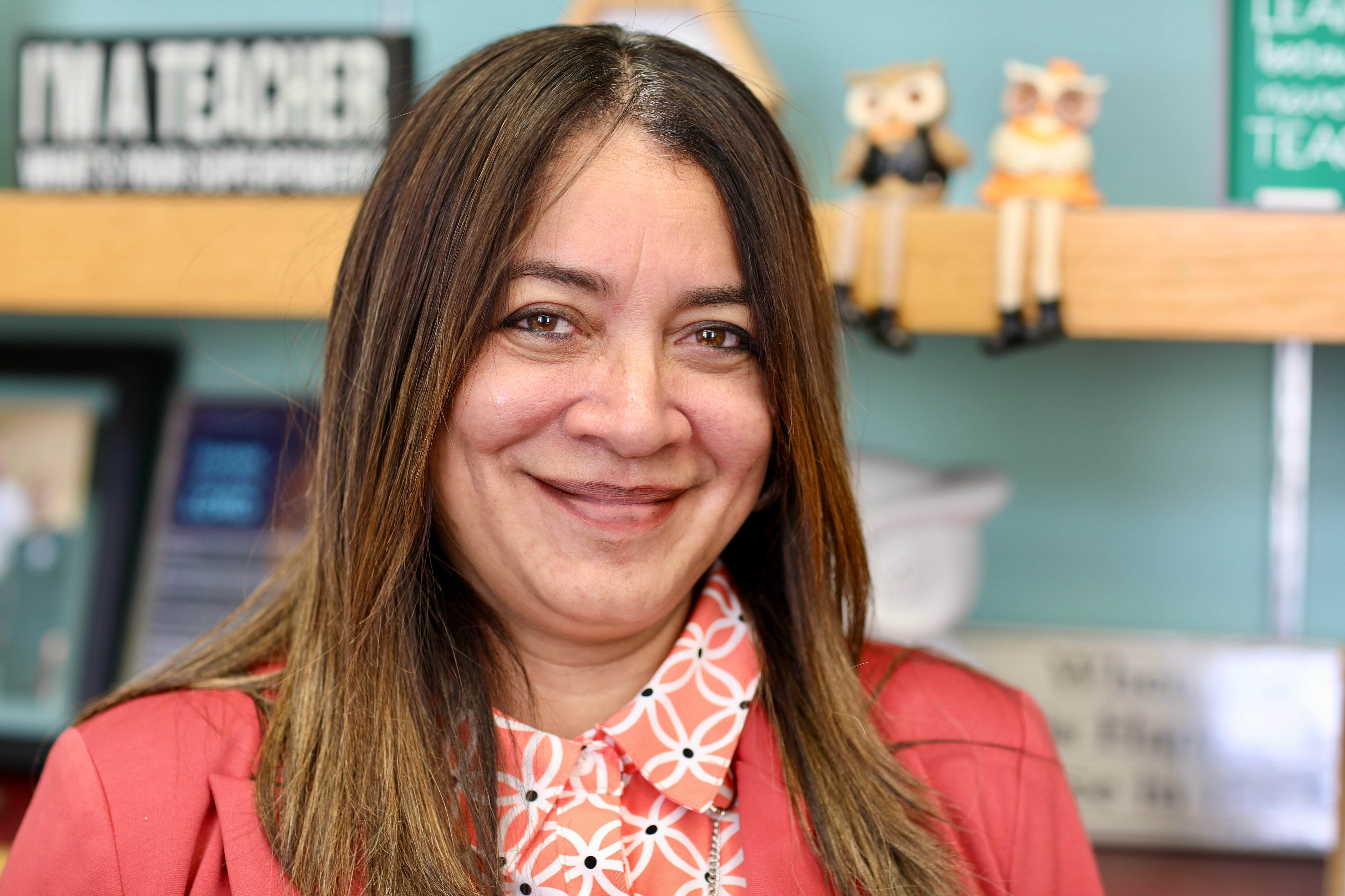 A woman with brown hair and an orange and white shirt and orange jacket smiles at the camera.
