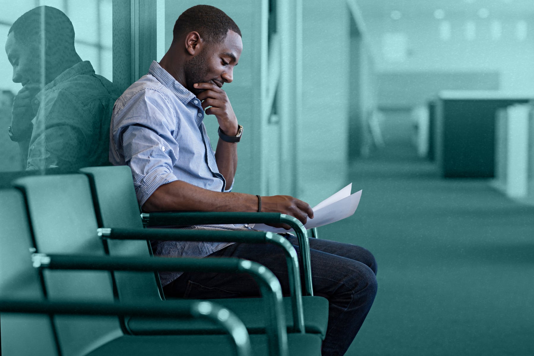 A man sitting on a chair reading over his resume while waiting to be interviewed for a teaching position.