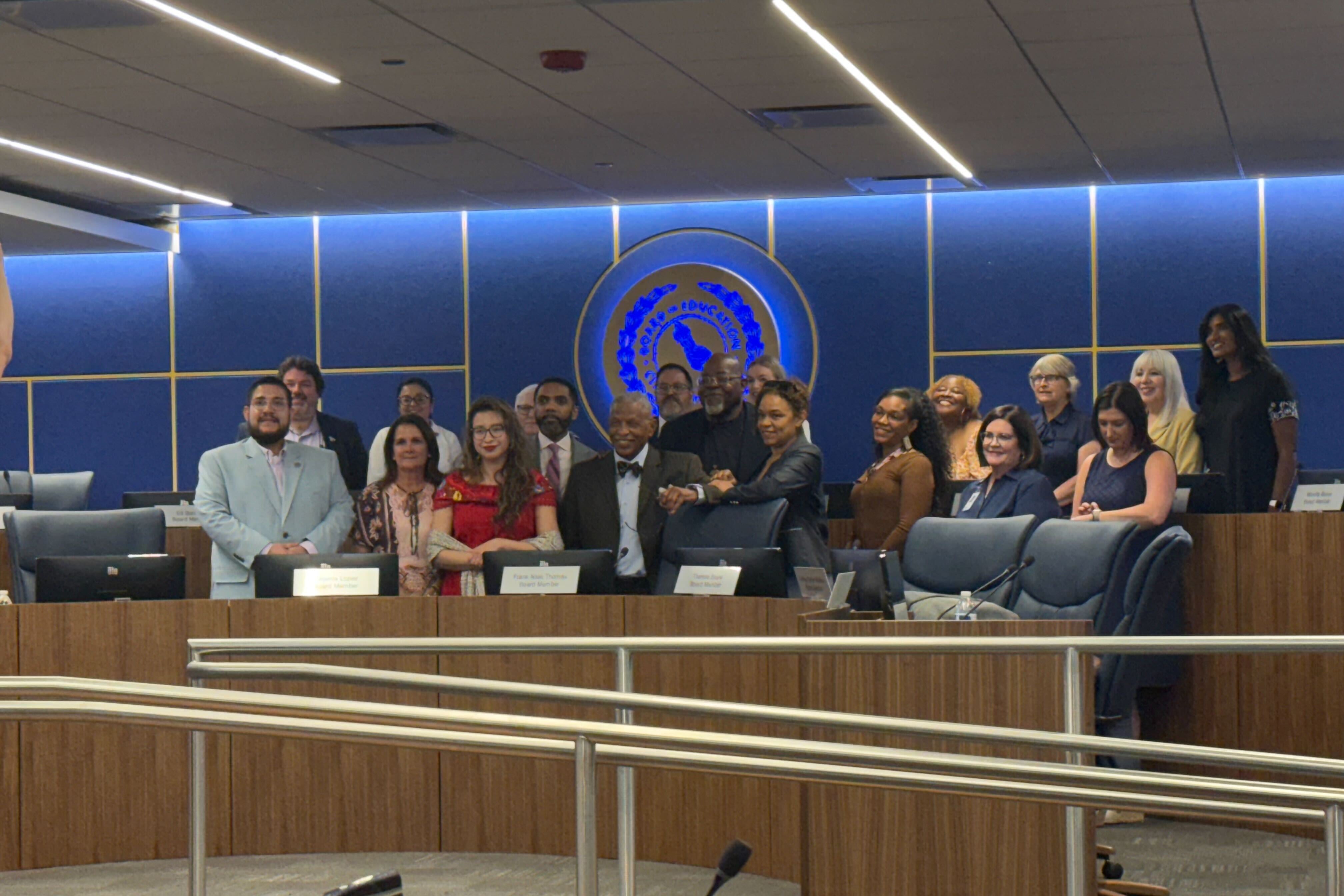 A group of adults in suits pose for a photograph in a large conference room.