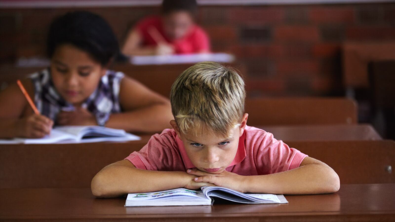 A young boy resting his head on his arms as he sits in a classroom looking bored (Getty Images)