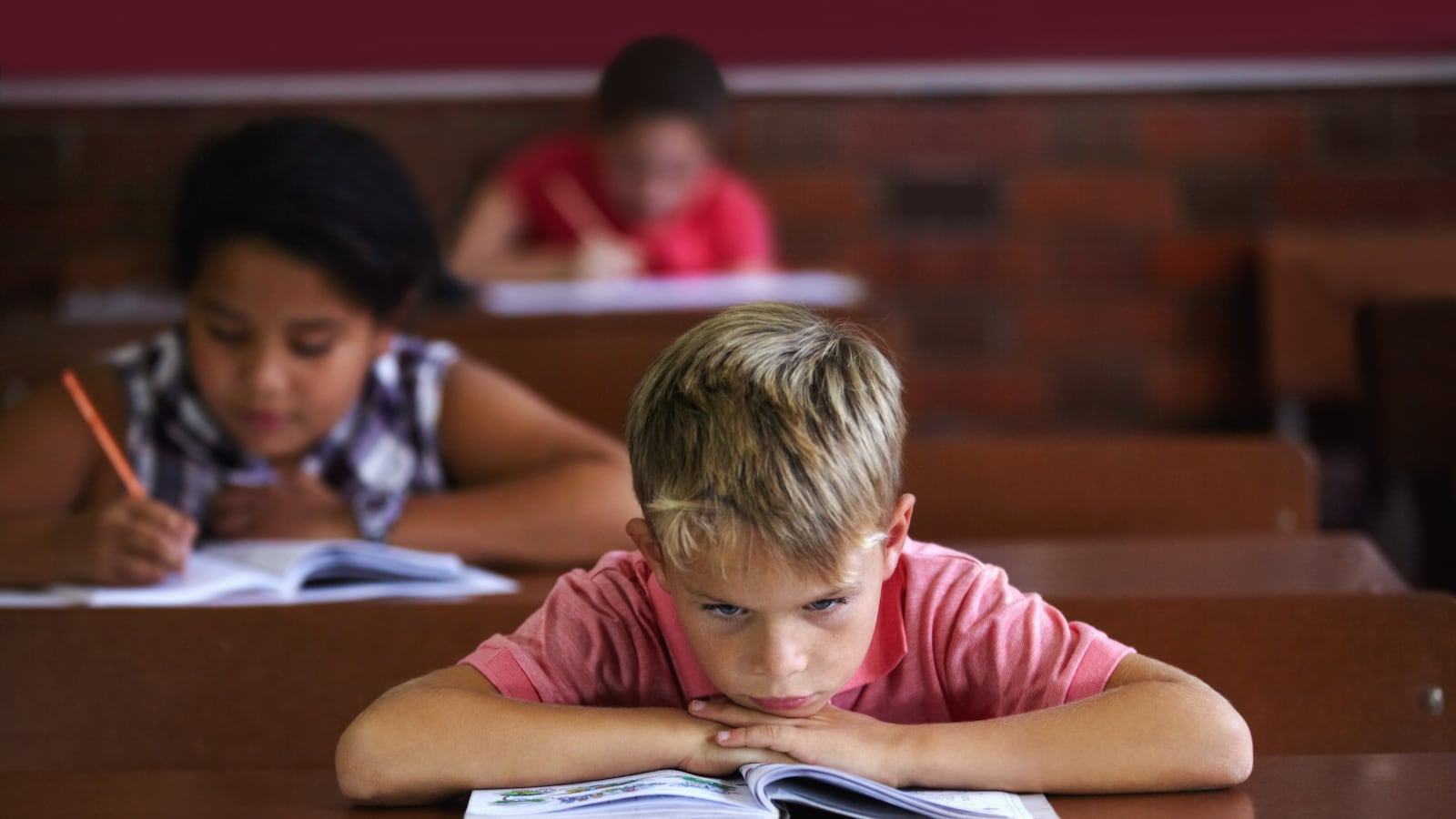 A young boy resting his head on his arms as he sits in a classroom looking bored (Getty Images)