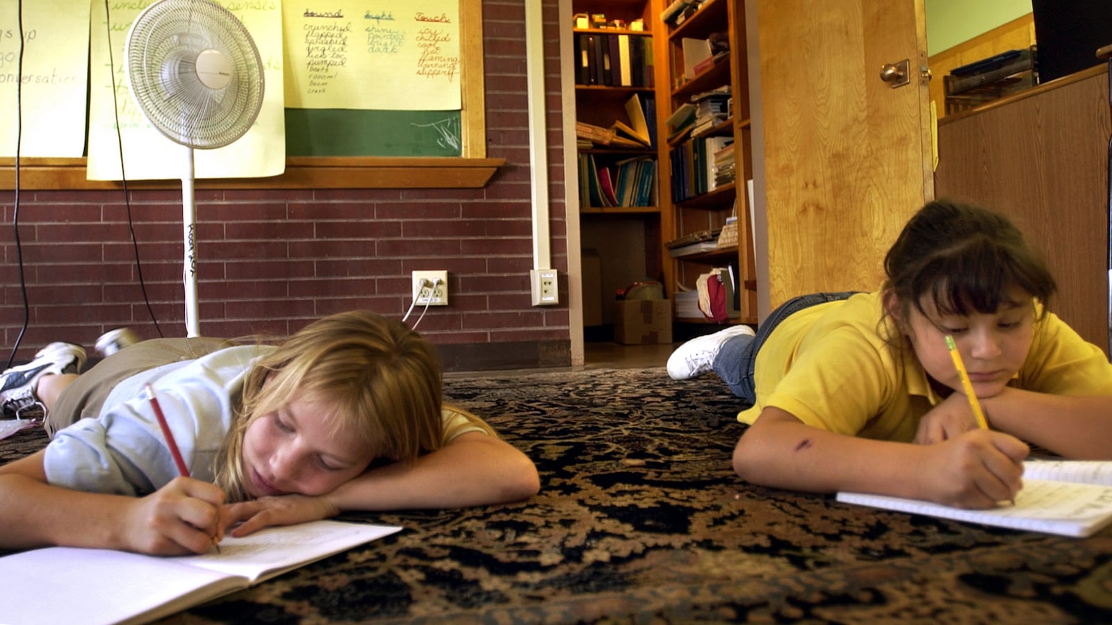 Darlene  Cisneros , 10, left, and Manuela  Ramirez , 10, of Harry M. Barrett Elementary School, Denver, Colo, is taking a note by the electric fan during the afternoon writing class on Tuesday afternoon in 2003.