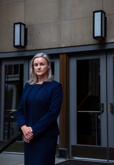 A woman wearing a dark dress poses for a portrait outside of a courthouse.