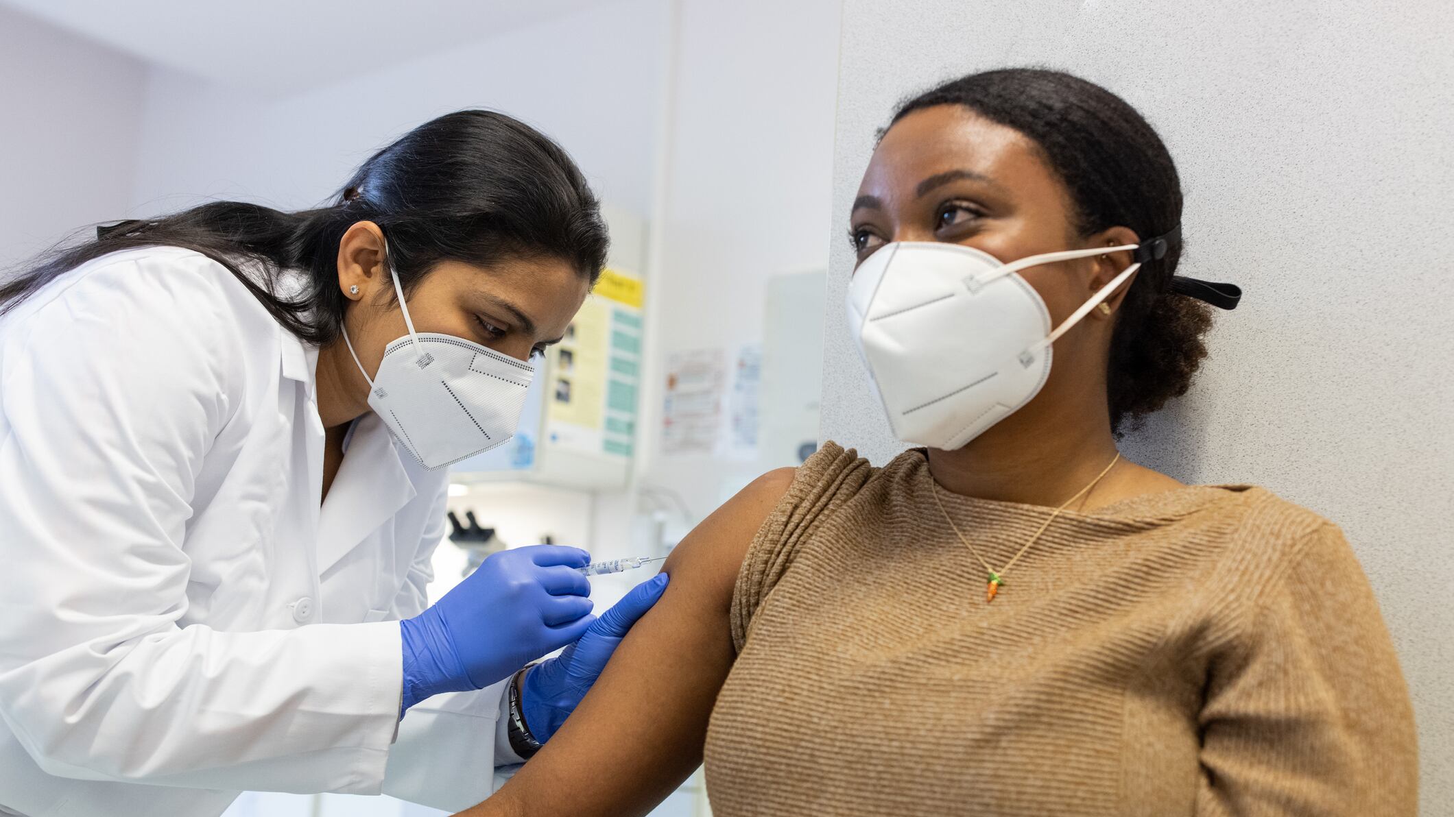 A masked woman receives a shot from a doctor.