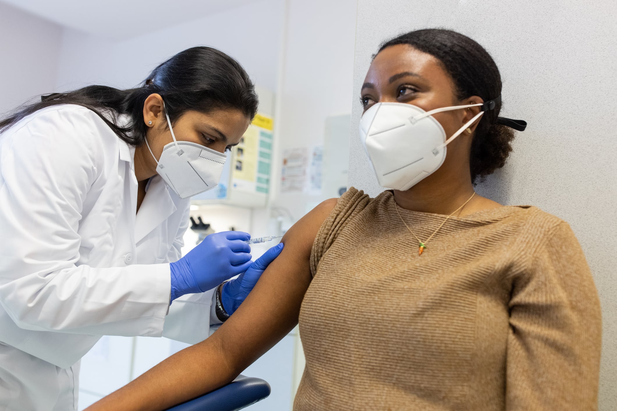 A masked woman receives a shot from a doctor.