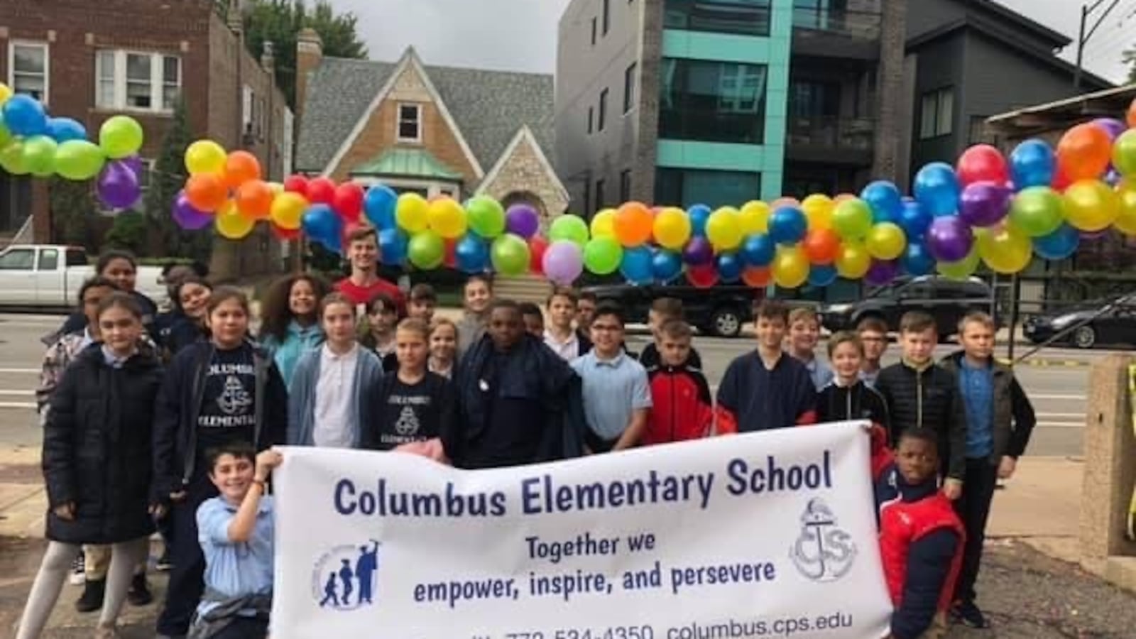 A group of students holds a sign that says Columbus Elementary School. 