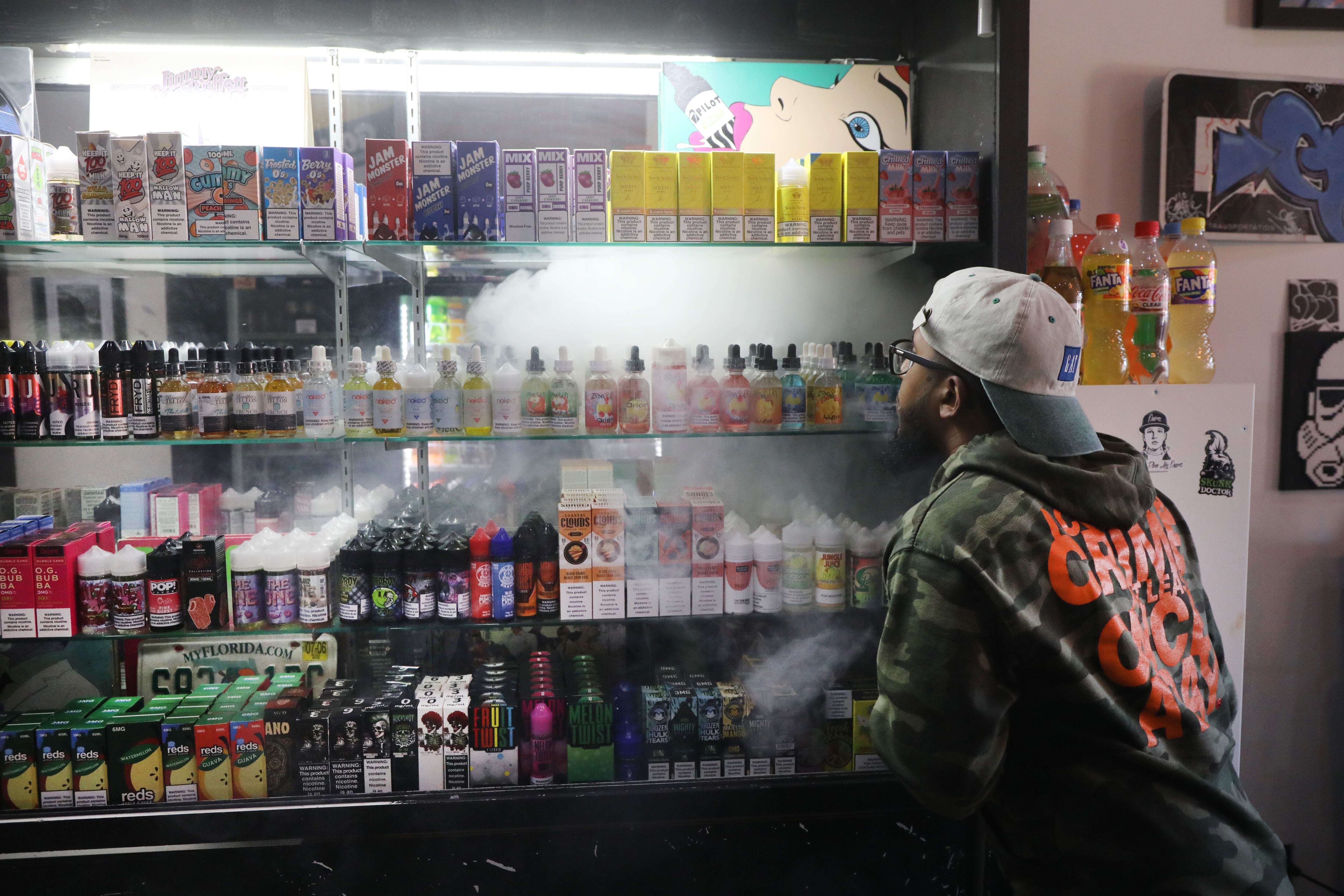 A worker in a vape story looks at shelves full of vaping merchandise with vape smoke in the air.