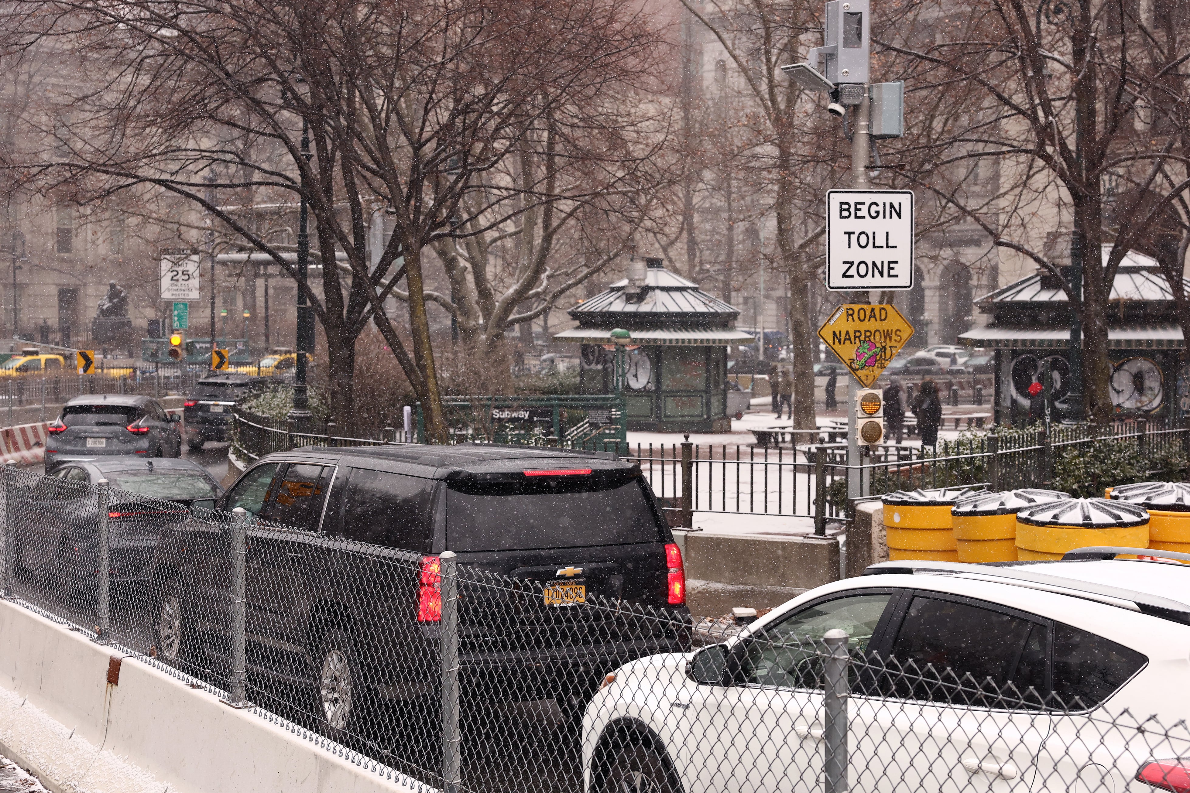 A line of cars in traffic with buildings and signs in the background.