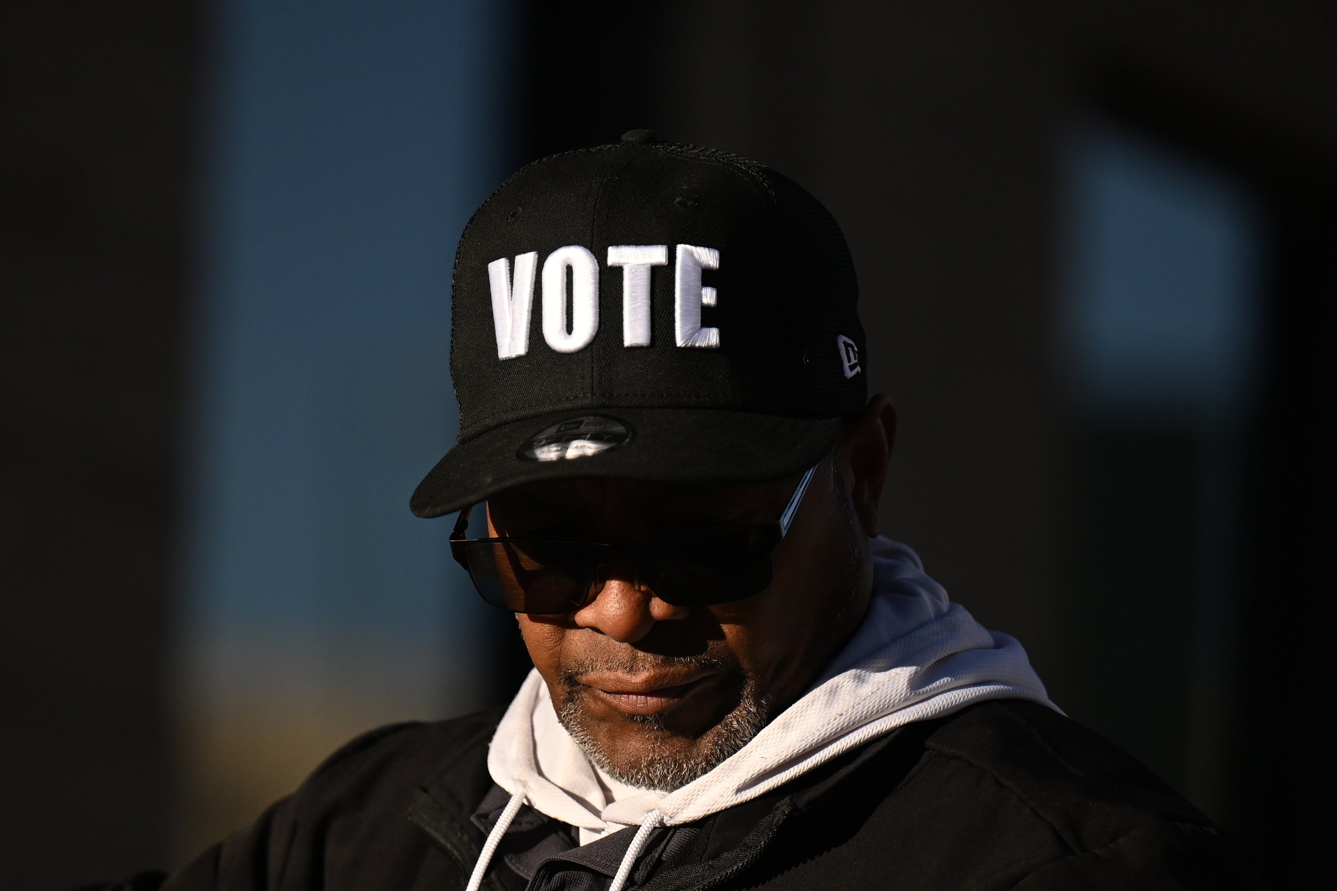 A photograph of a Black man wearing a baseball hat that reads "VOTE" stands outside.