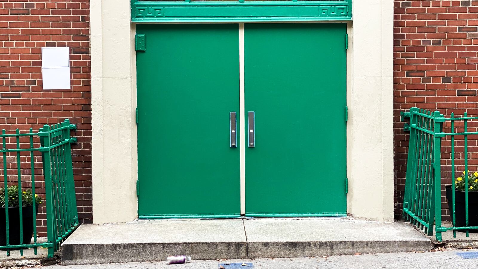 The outside of a brick school building with green doors.