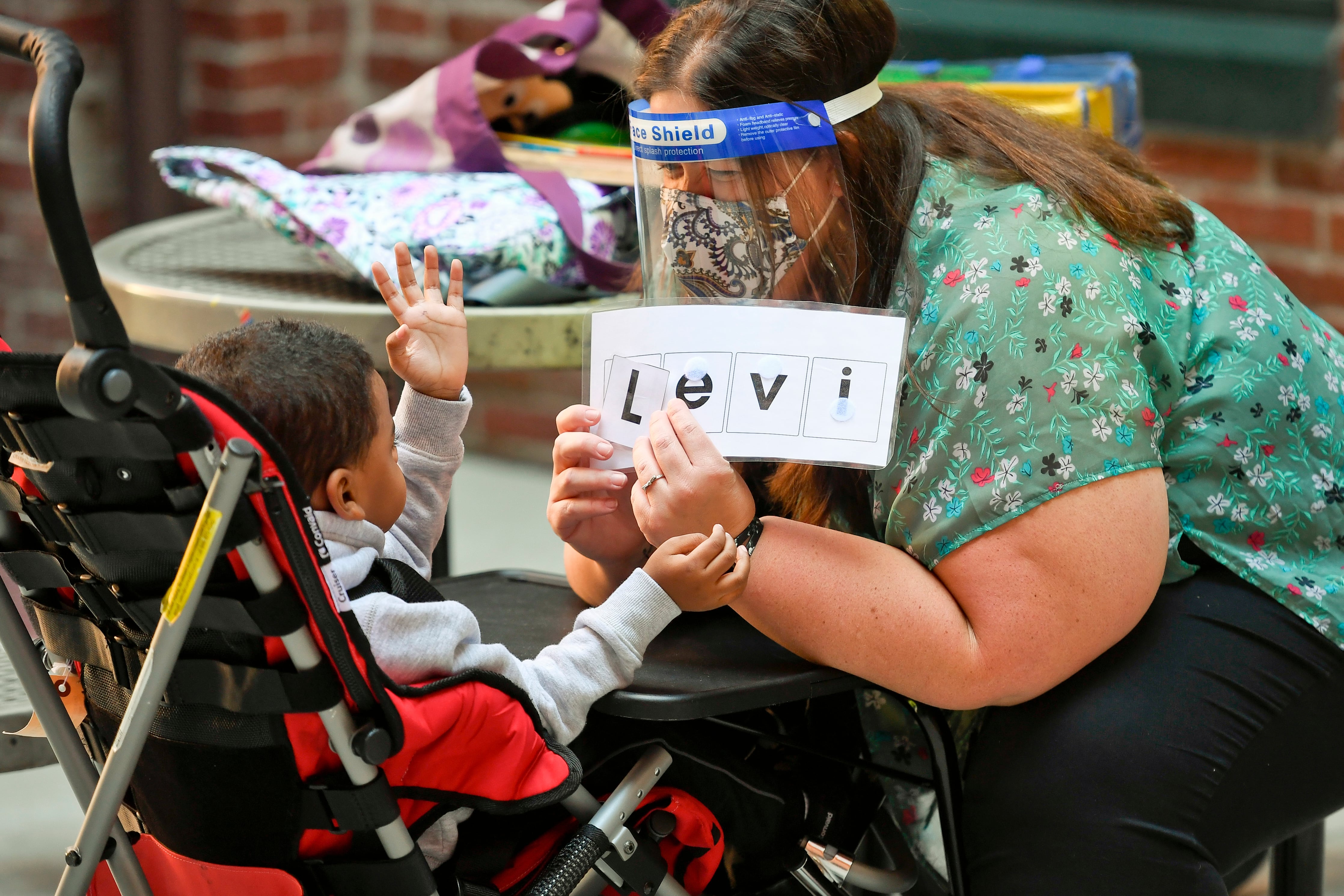 A special educator works with one of her students, wearing a face shield and protective mask.