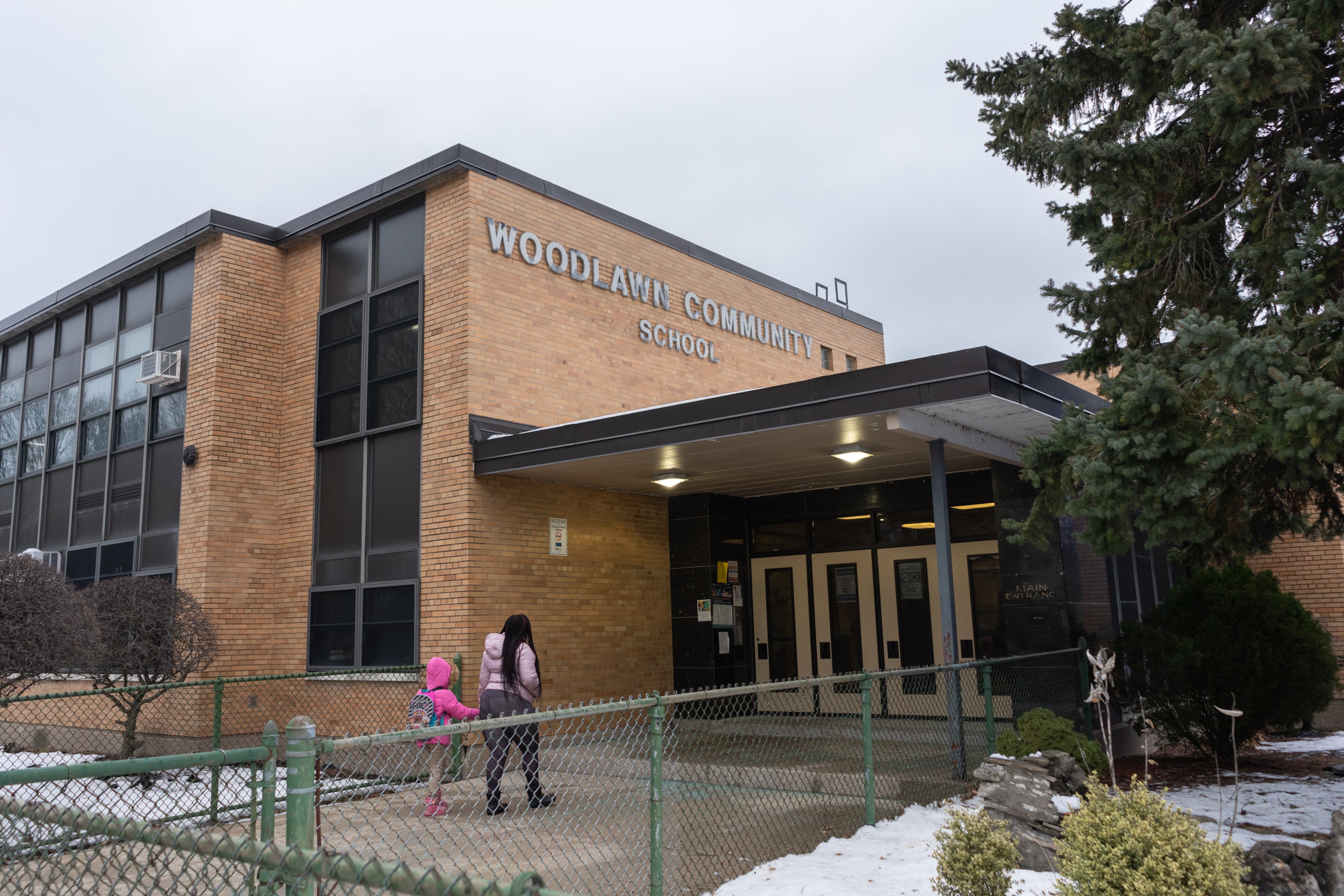 A mother and daughter, wearing winter clothing, walk to the entrance of Woodlawn Community School in Chicago.