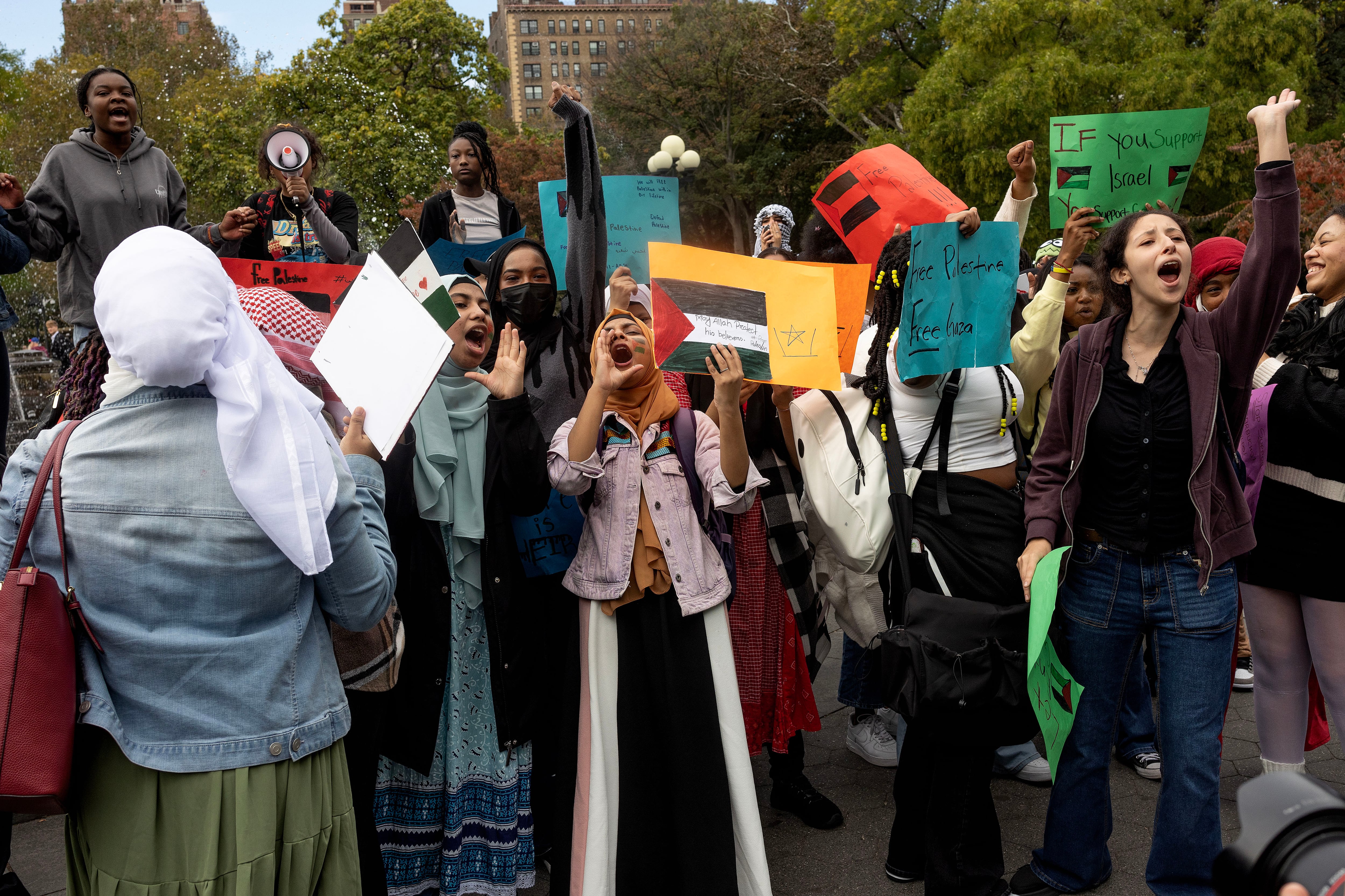 A group of young people chant, hold signs while protesting outside.