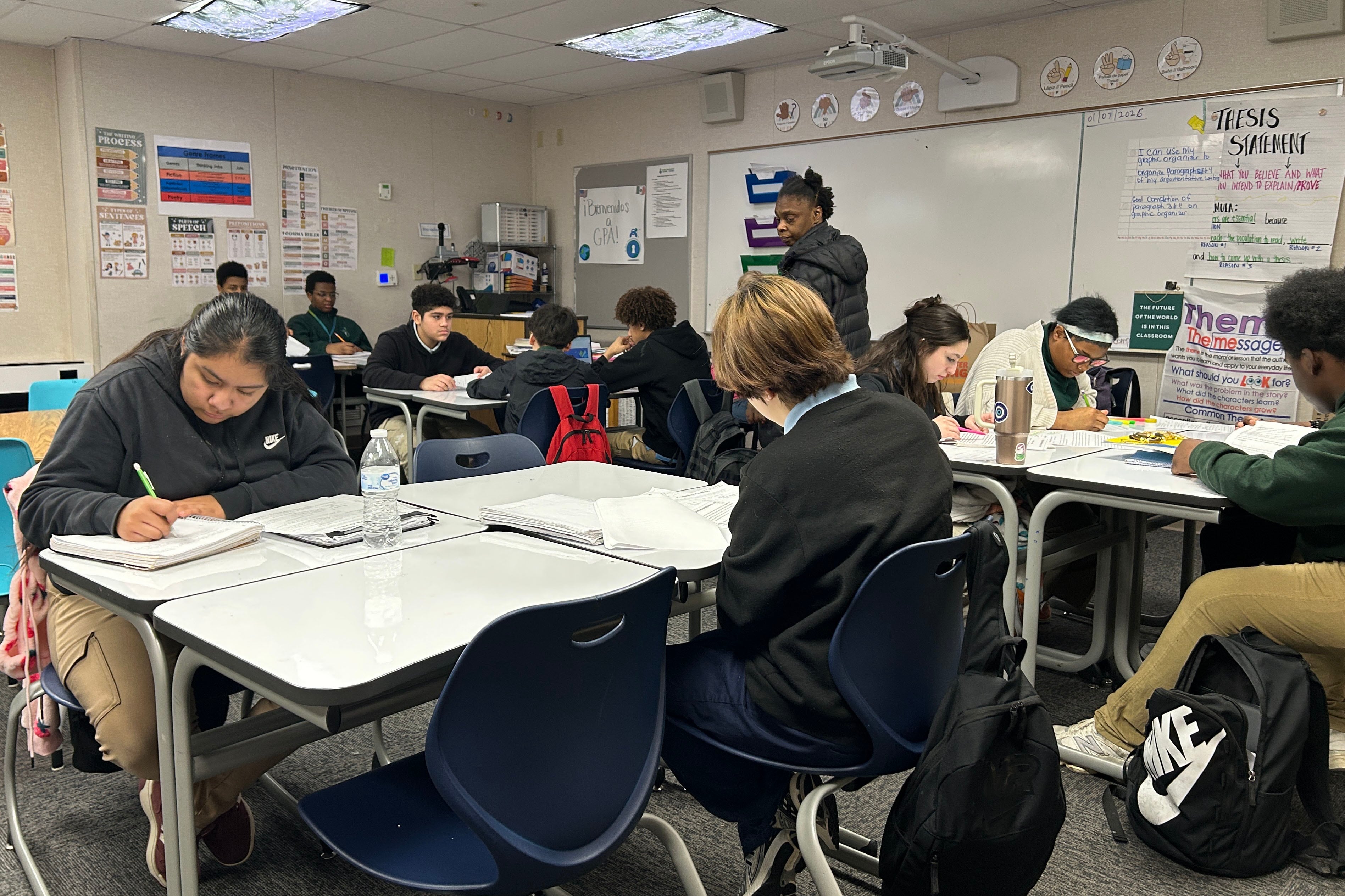 A photograph of a middle school classroom full of students sitting at their desks and a teacher in the background.