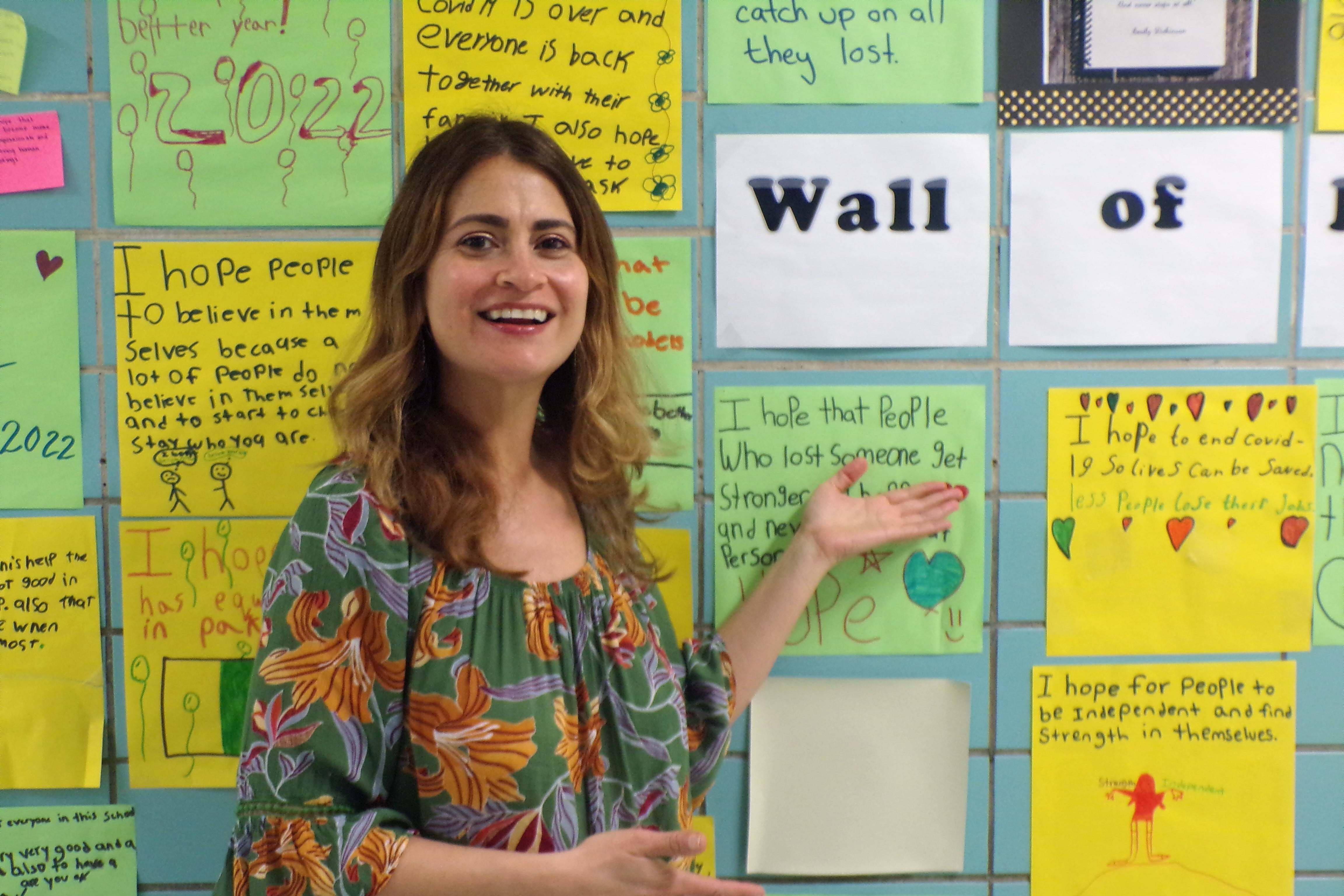 A woman shows off student work featured on a classroom wall.