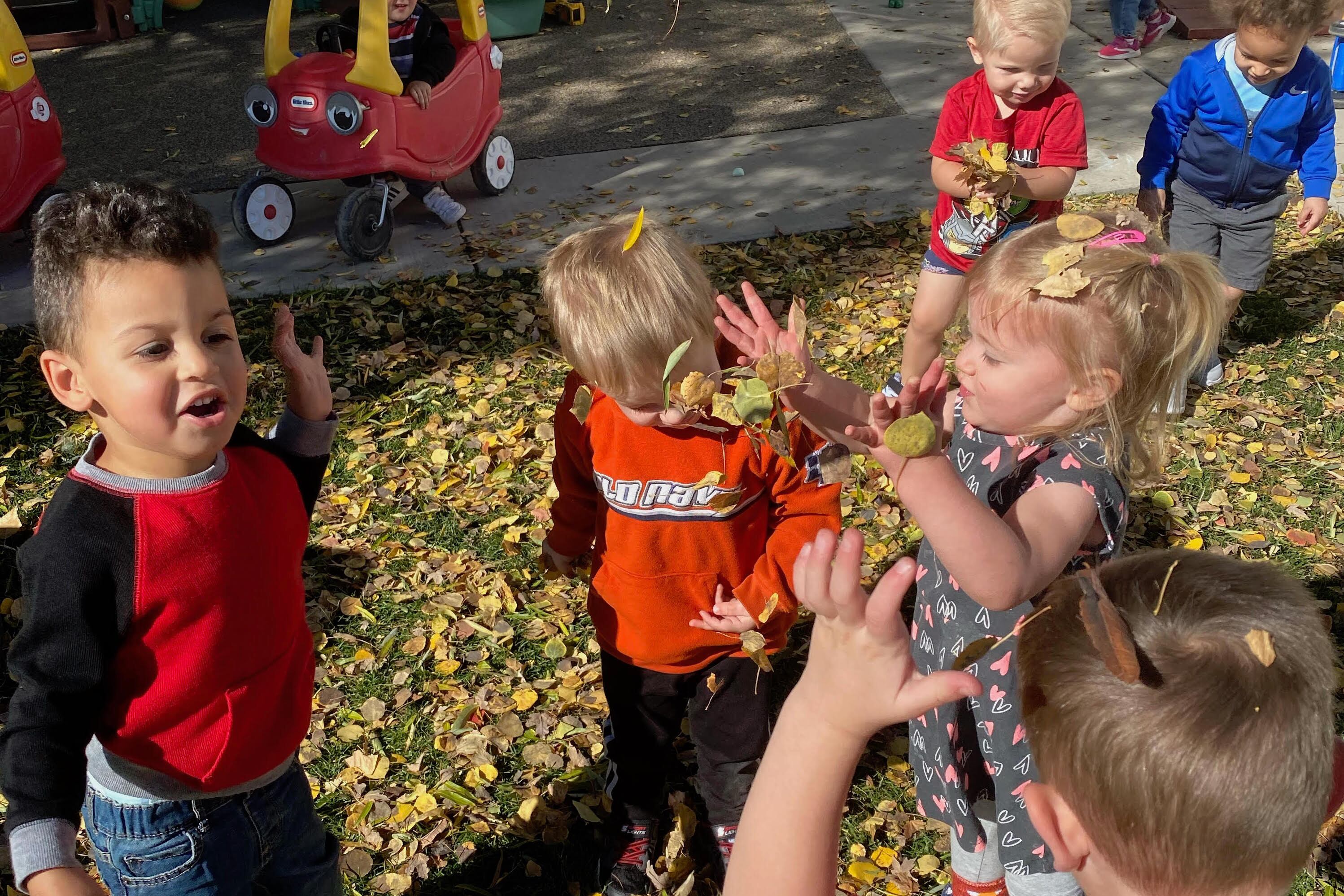 Six preschool children play in fall leaves
