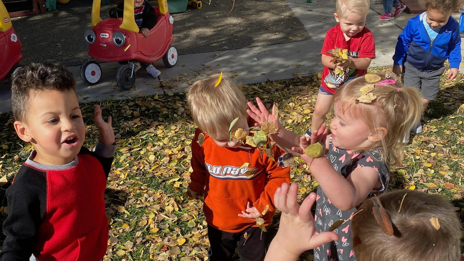 Six preschool children play in fall leaves